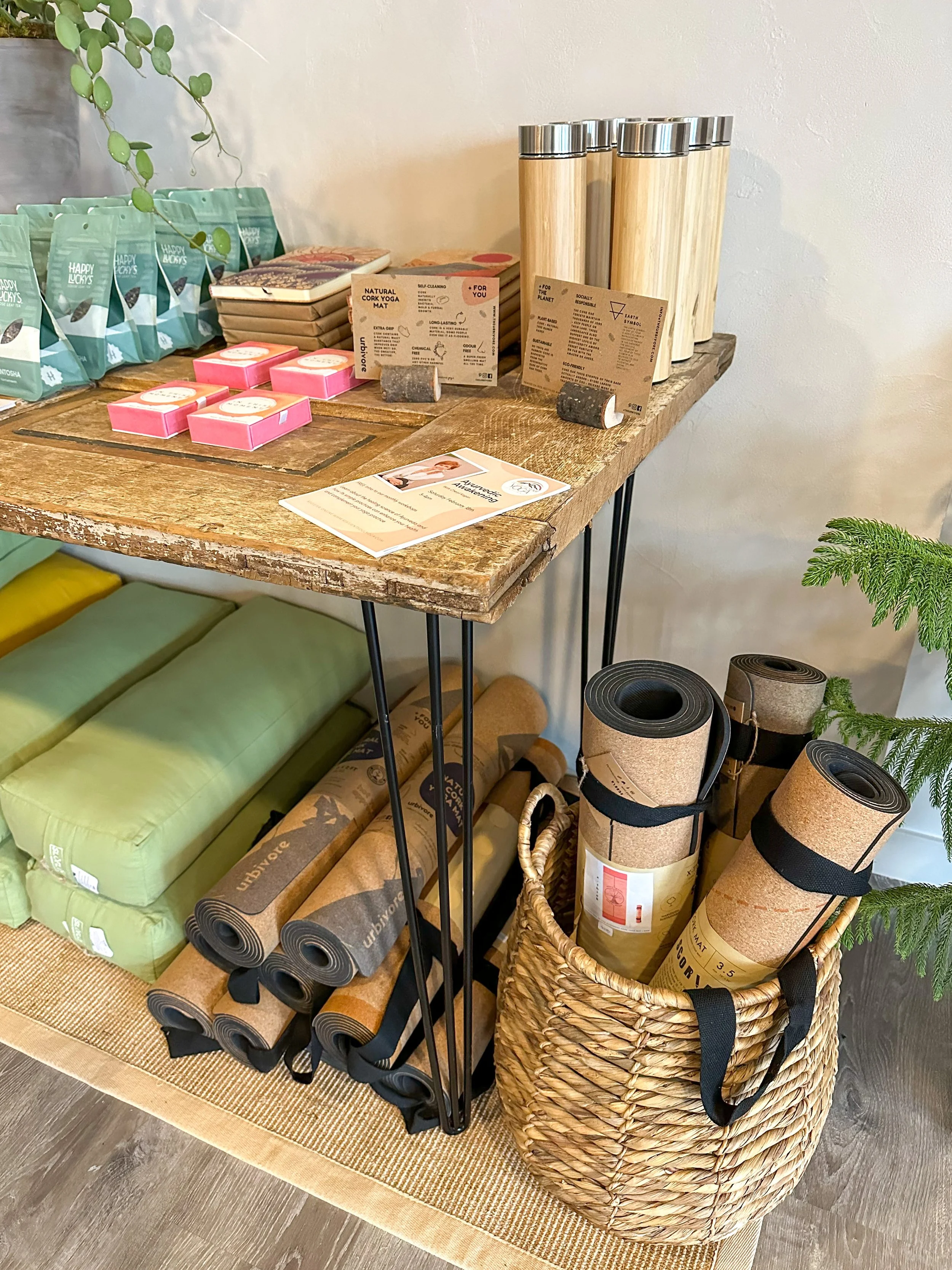 A wooden table displaying stress relief items, including herbal teas, natural candles, and yoga mats in a basket, with a small plant and promotional flyer nearby.