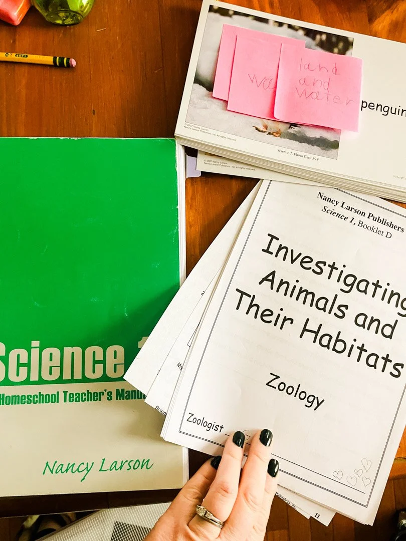 NLS Guide, booklet with the words "investigating animals and their habitats, and a stack of animal picture cards with a post it in a child's handwriting that reads "land and water"