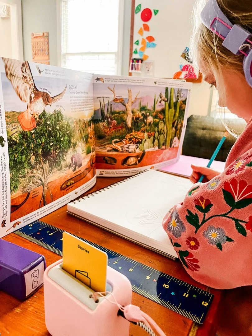 child drawing with a habitats book propped up
