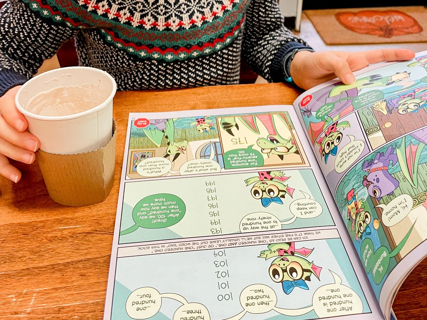 child reading Beast Academy math comic book with cup of hot cocoa