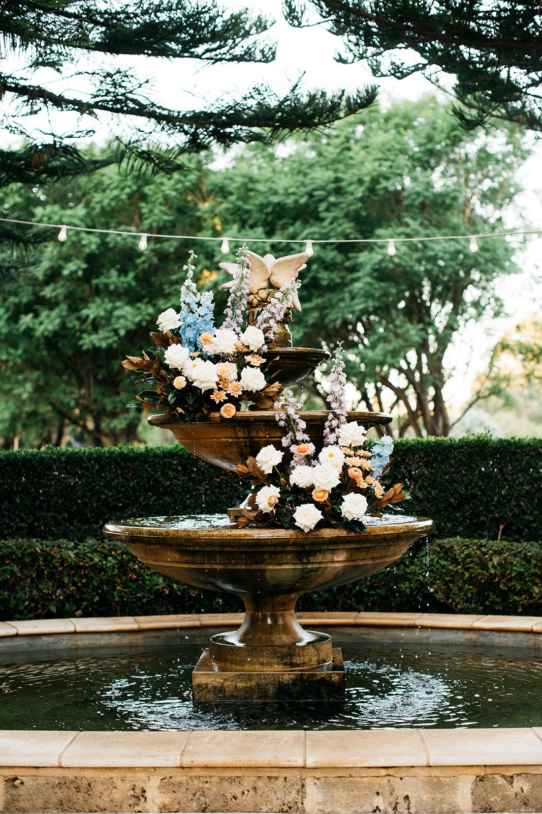 Decorative fountain with flowers and a butterfly sculpture in an outdoor garden setting.