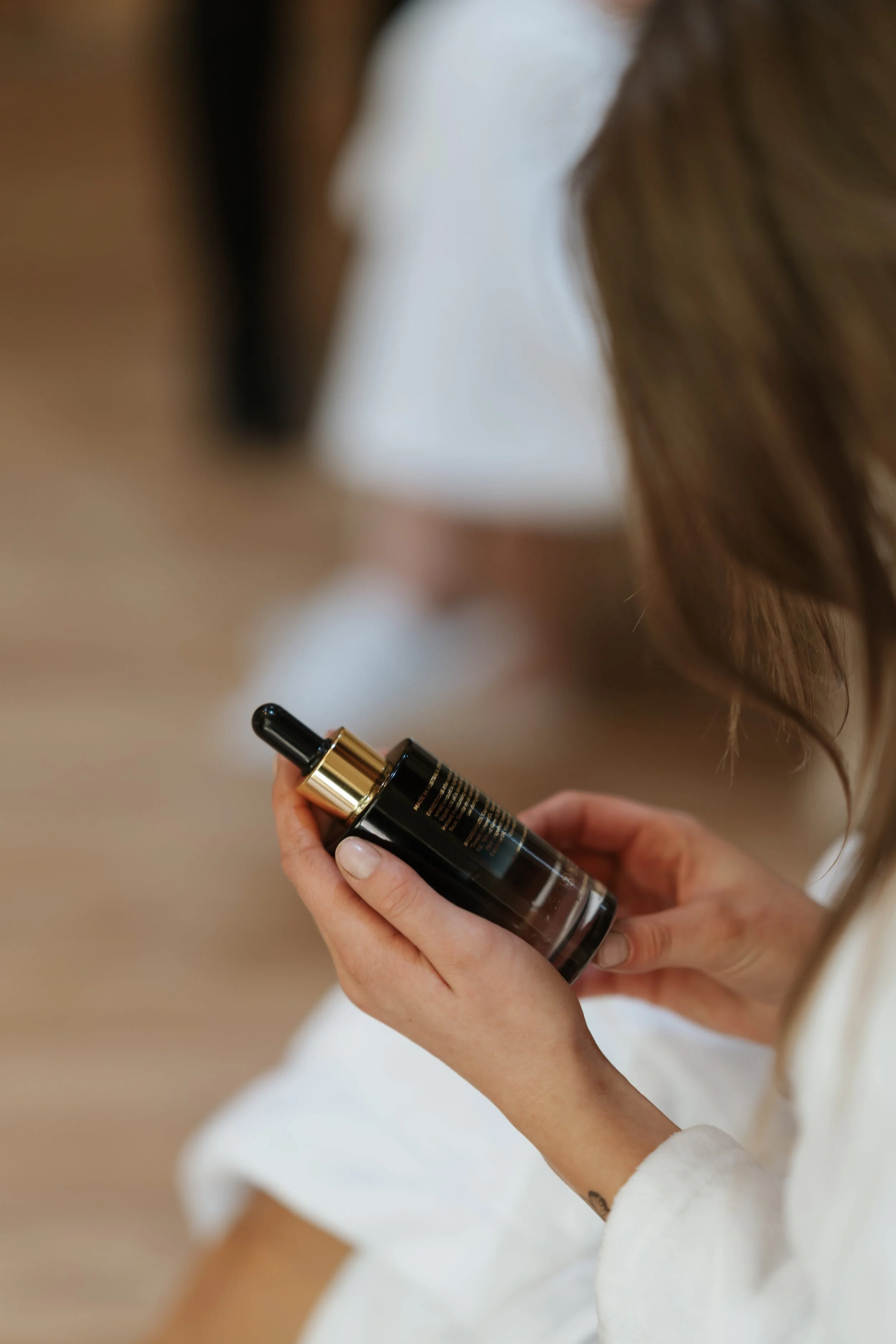 A woman in a white robe holding a black bottle with a dropper cap.