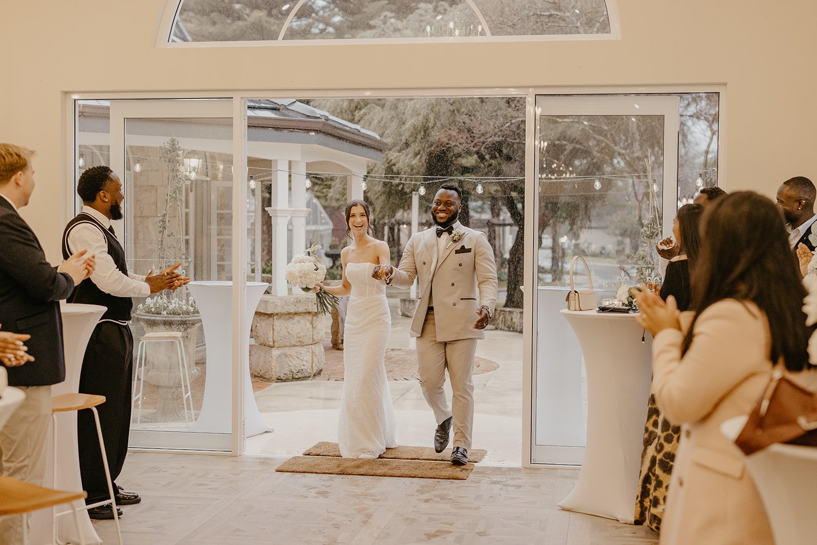 Happy bride and groom walking into the wedding reception as guests applaud.