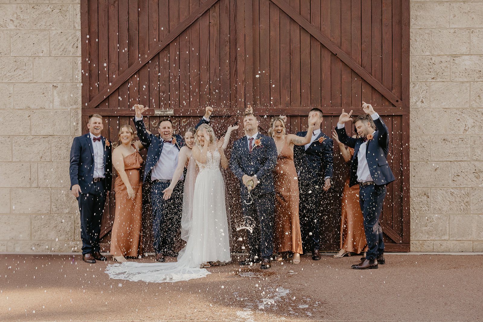 A group of people celebrating at a wedding, throwing confetti outside near a wooden gate.