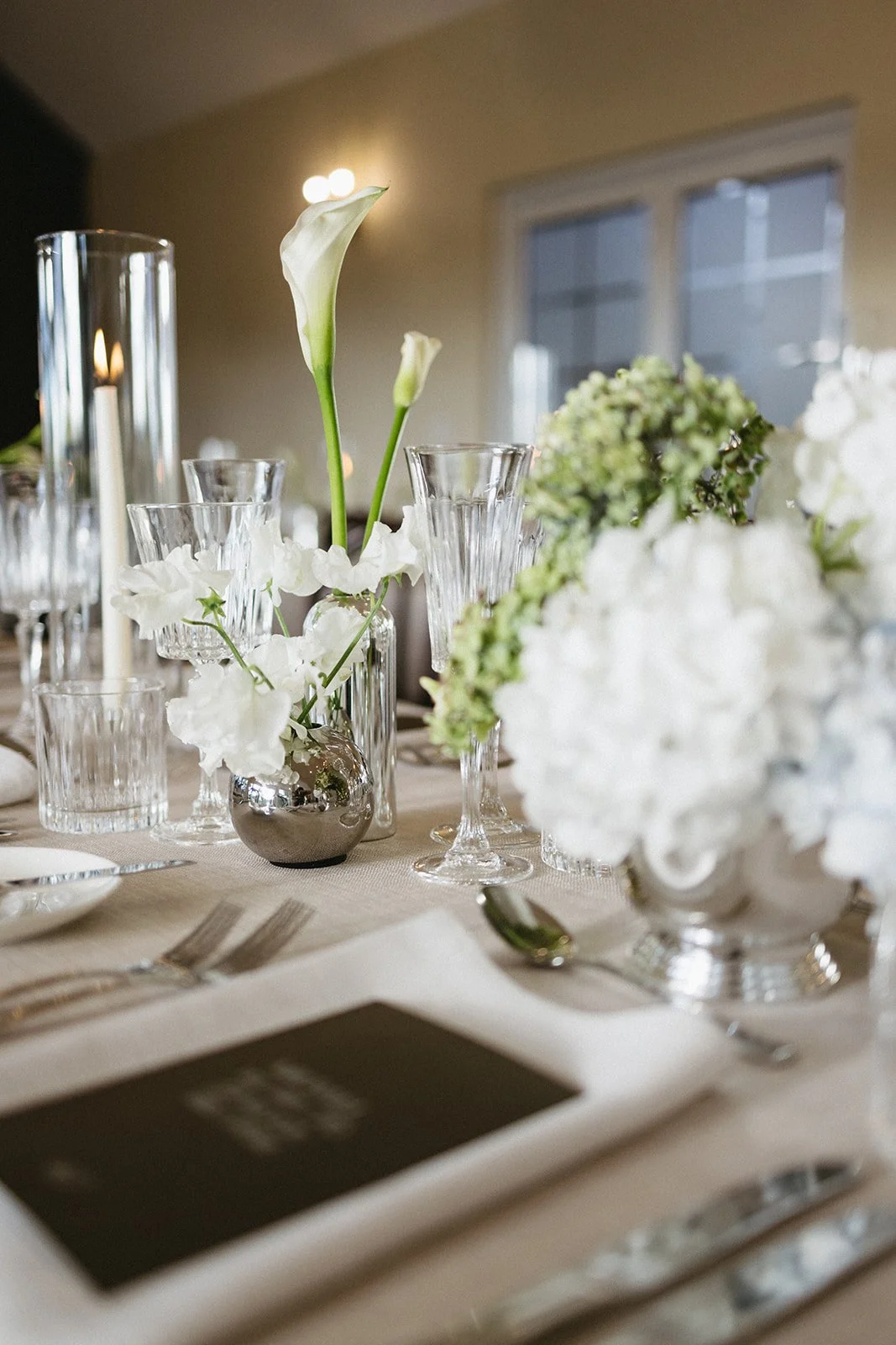 Elegant dining table decorated with white flower arrangements, clear glassware, and silver accents, set for a formal event.