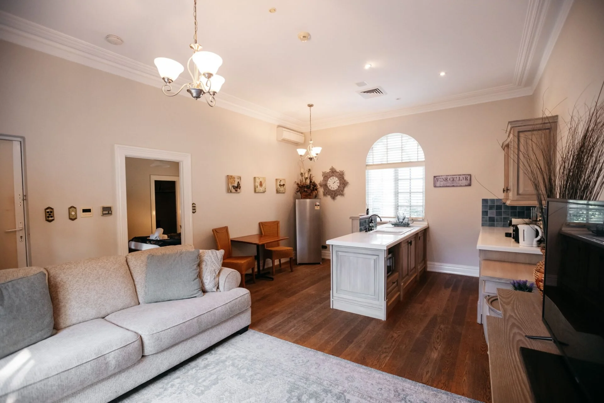 Living room and kitchen area in a home with beige walls, wooden floors, a beige sofa, wall decor, a kitchen island, and appliances.