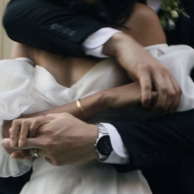 Close-up of a couple dancing closely, with the man in a dark suit and the woman in white, holding hands and embracing.