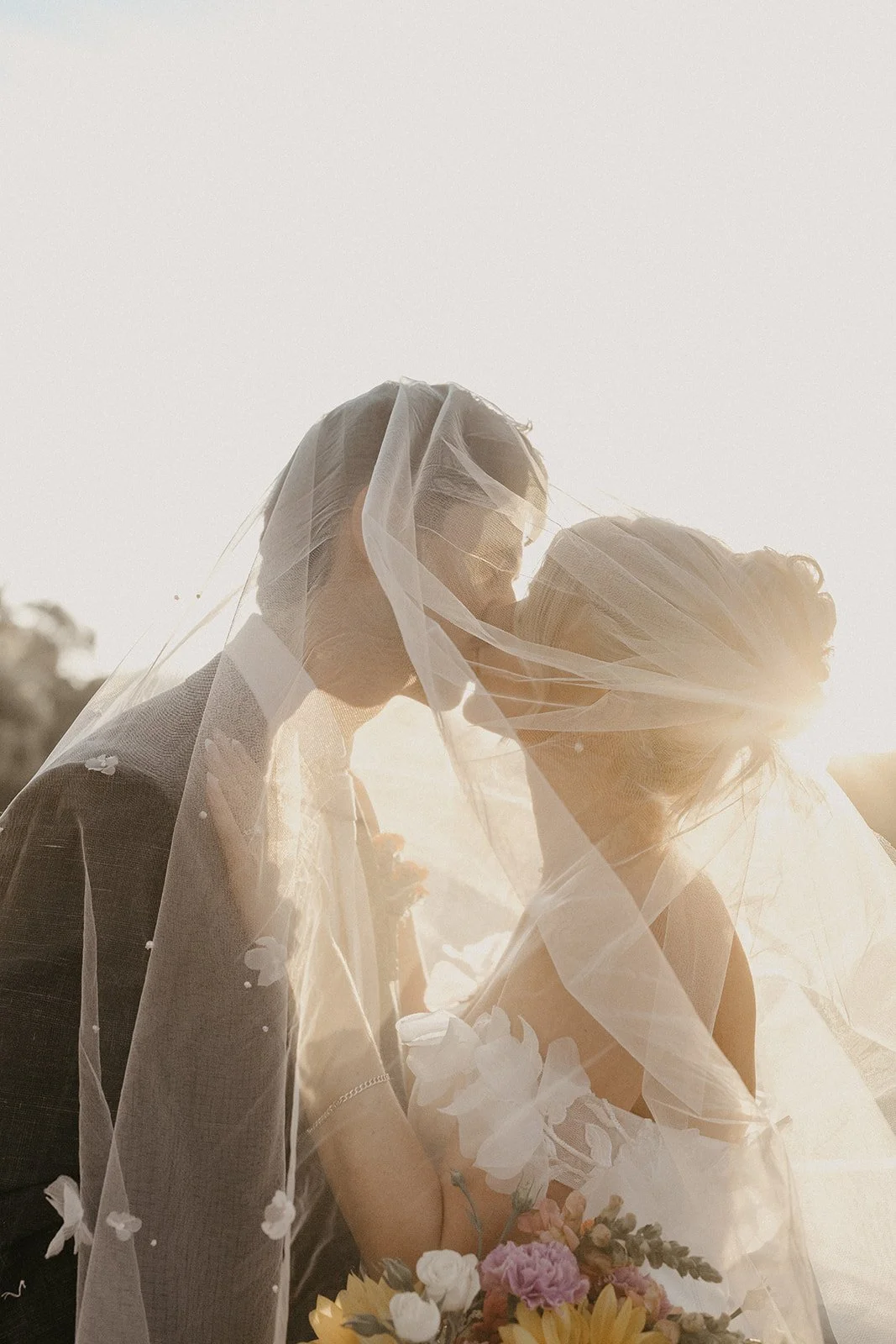 Bride and groom kissing under a veil at sunset, holding a bouquet of flowers in the Swan Valley Perth at Brookleigh Estate