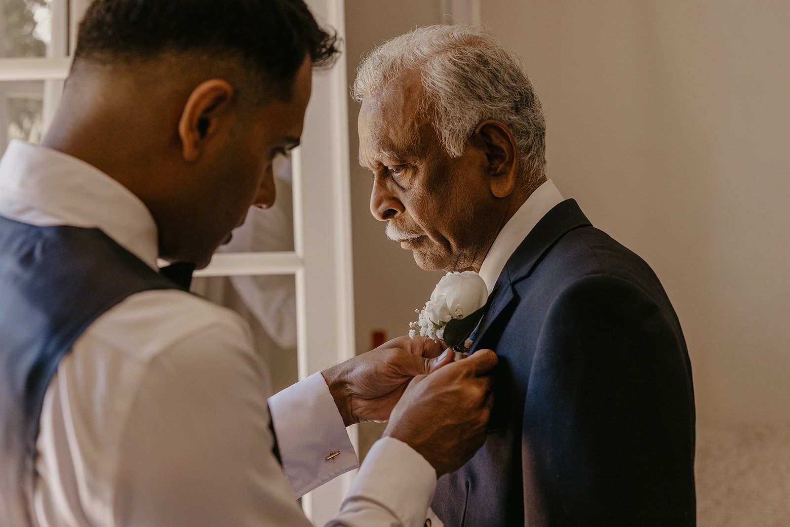 A young man pins a boutonniere on an older man's tuxedo, likely for a formal event or wedding.