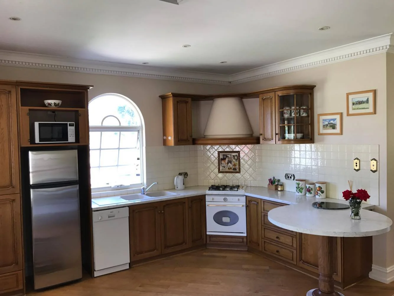 Kitchen with wooden cabinets, white countertop, window, microwave, refrigerator, oven, stove, and kitchen decor.