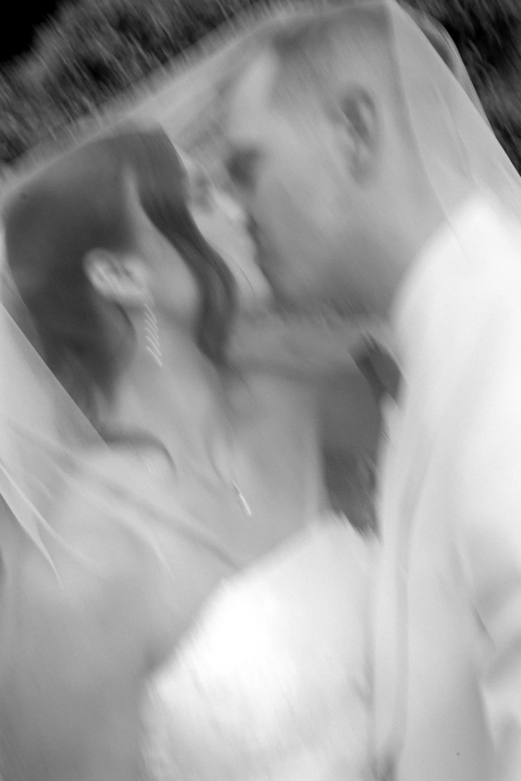 A black and white photo of a man and woman facing and leaning into each other, about to kiss, behind a transparent veil.