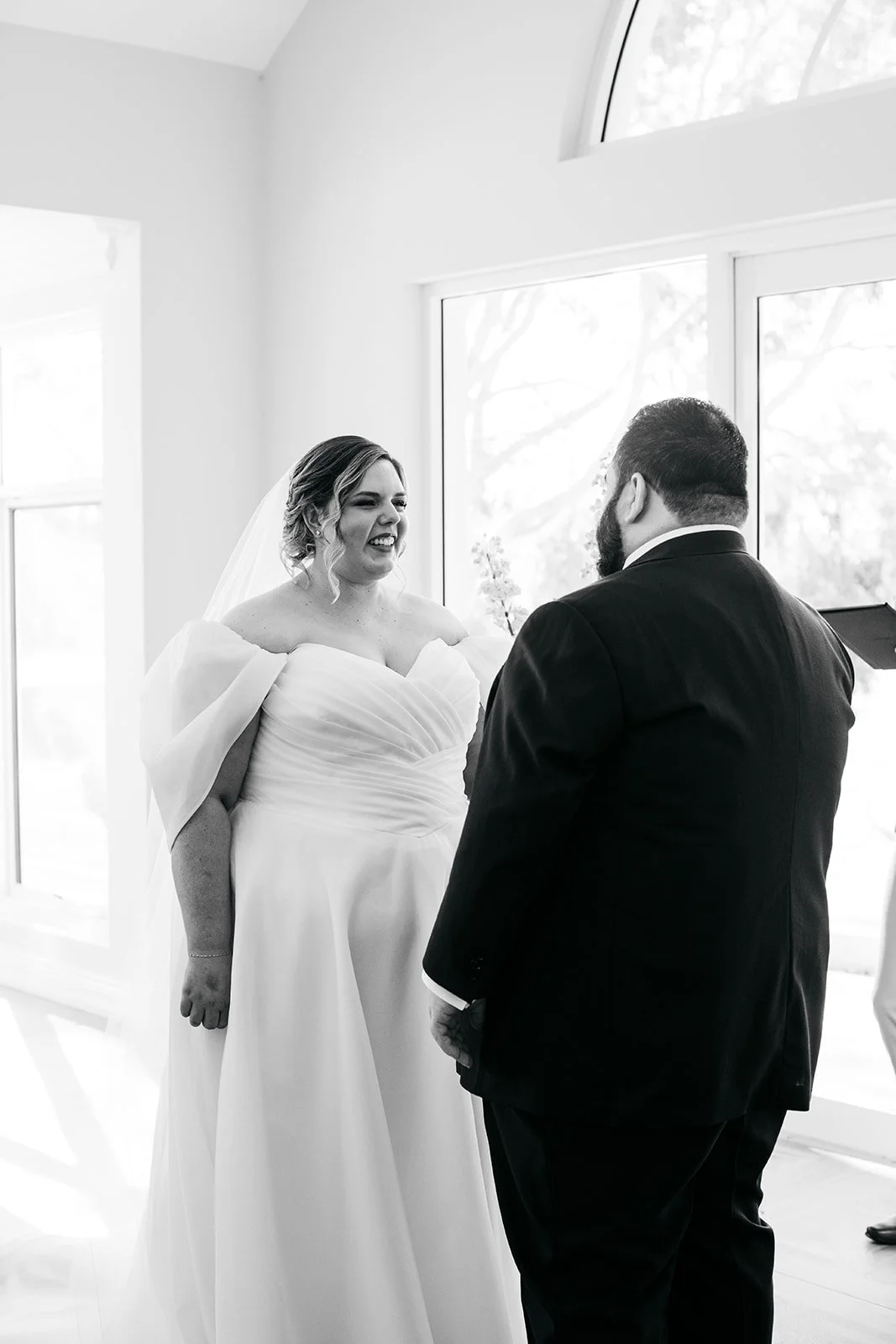 A bride in a wedding dress smiling and talking with a groom in a suit during their wedding ceremony.