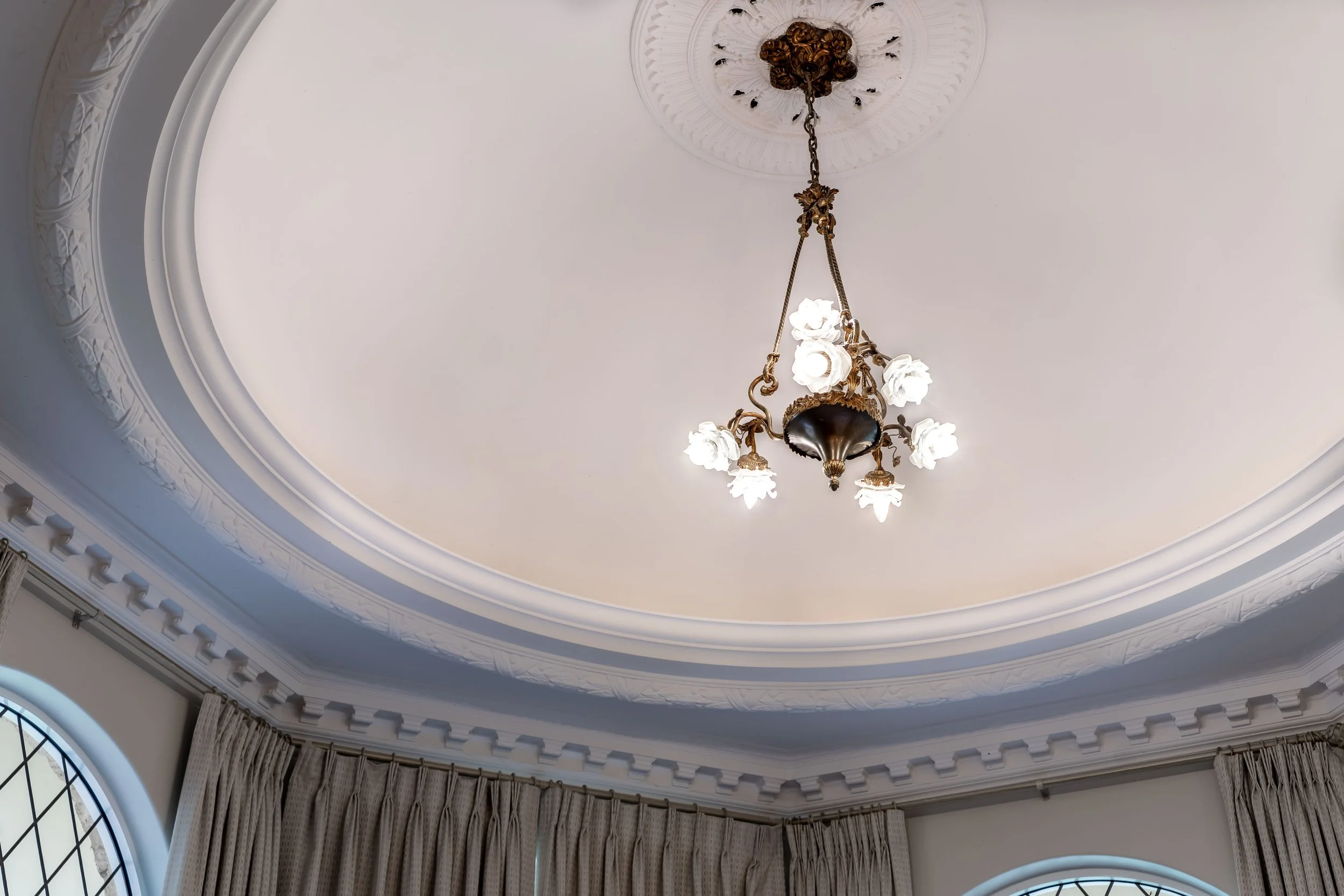 A ceiling with ornate crown molding, a decorative medallion, and a traditional chandelier with multiple floral-shaped light fixtures hanging from a chain.