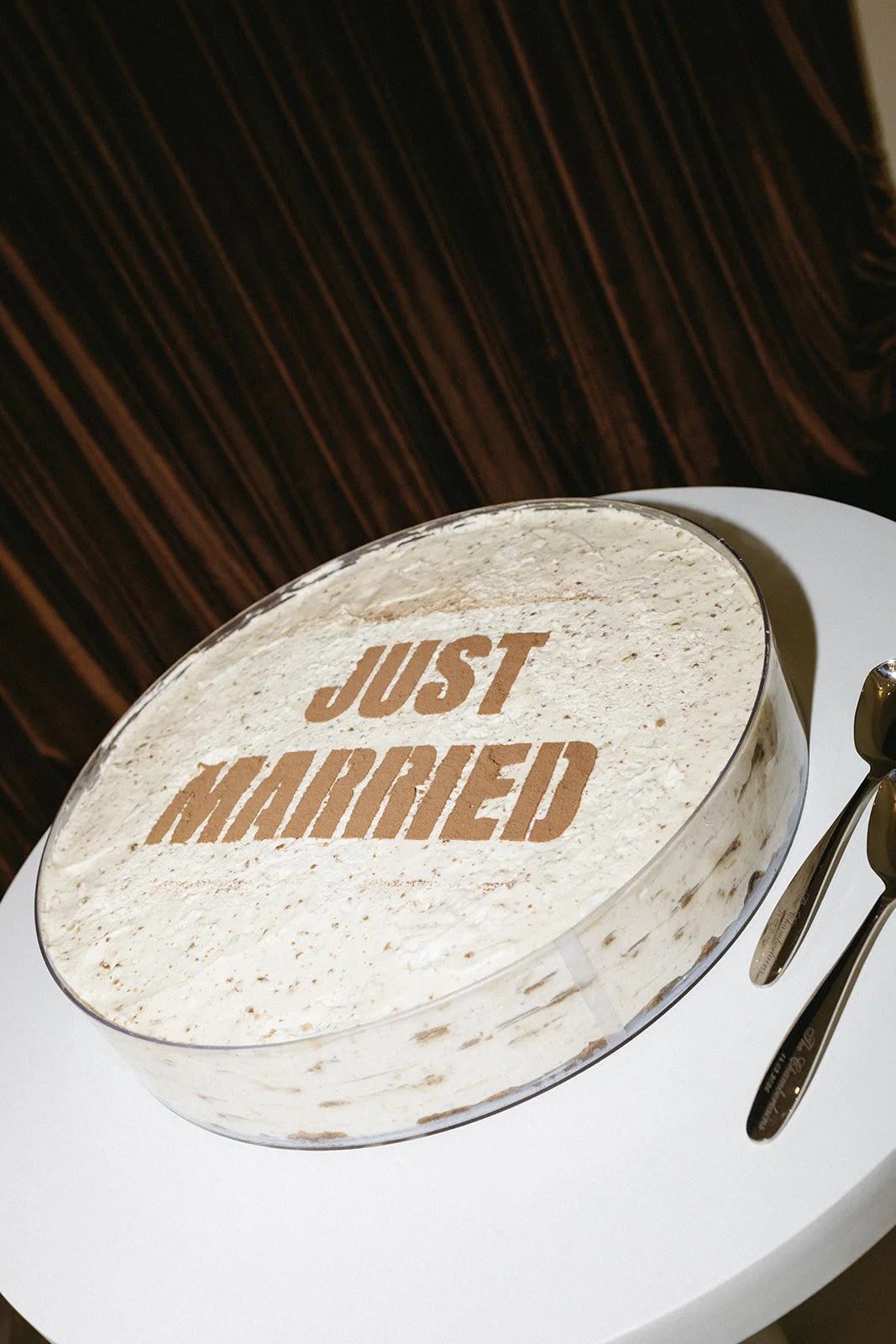 A cake with the words "JUST MARRIED" written on top and two forks placed beside it on a white surface.