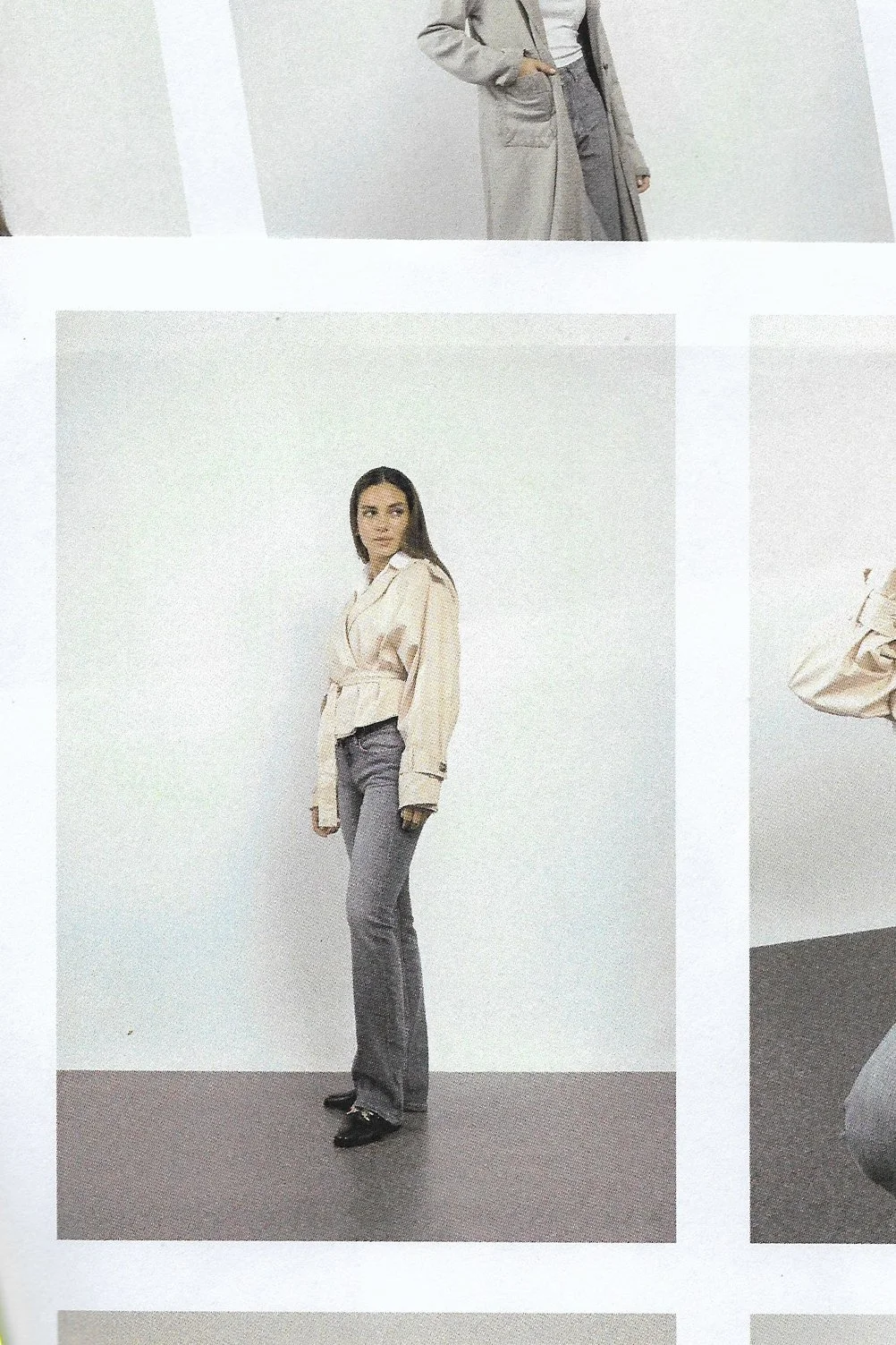 A woman with long dark hair wearing a beige blouse with puffed sleeves, gray flared pants, and black shoes, standing against a plain white wall.