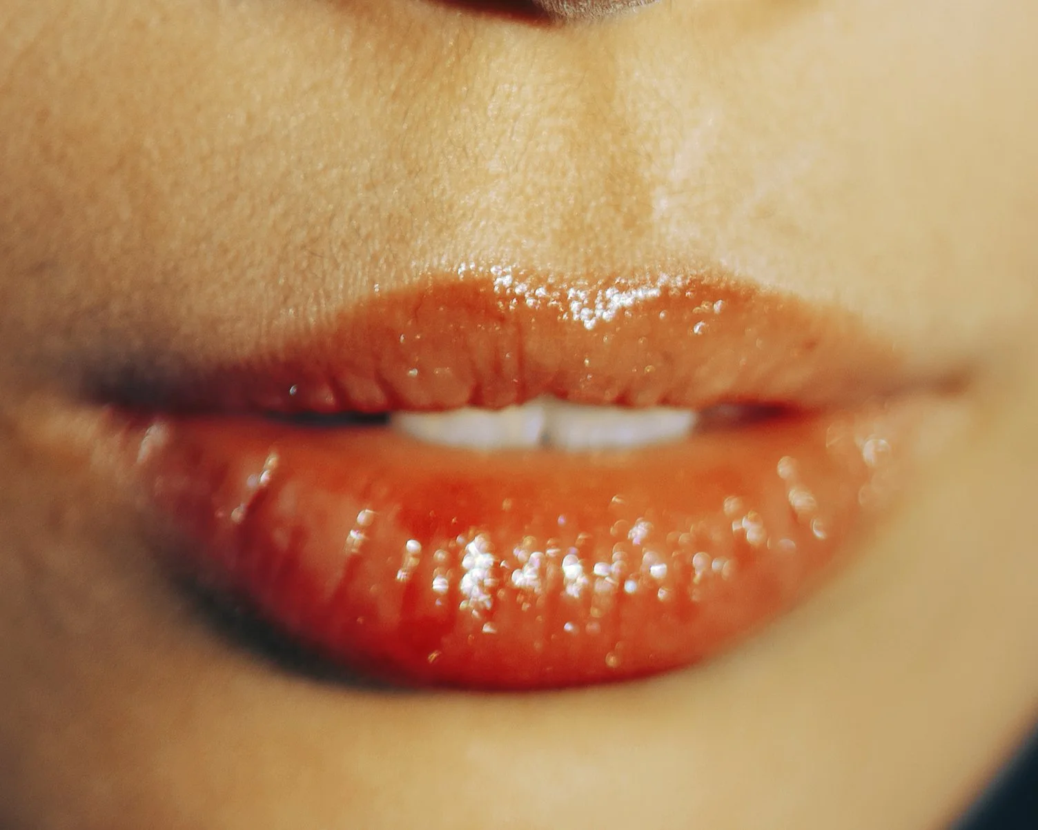 Close-up of a person's lips painted with vibrant orange lipstick, with some teeth visible between the slightly parted lips.