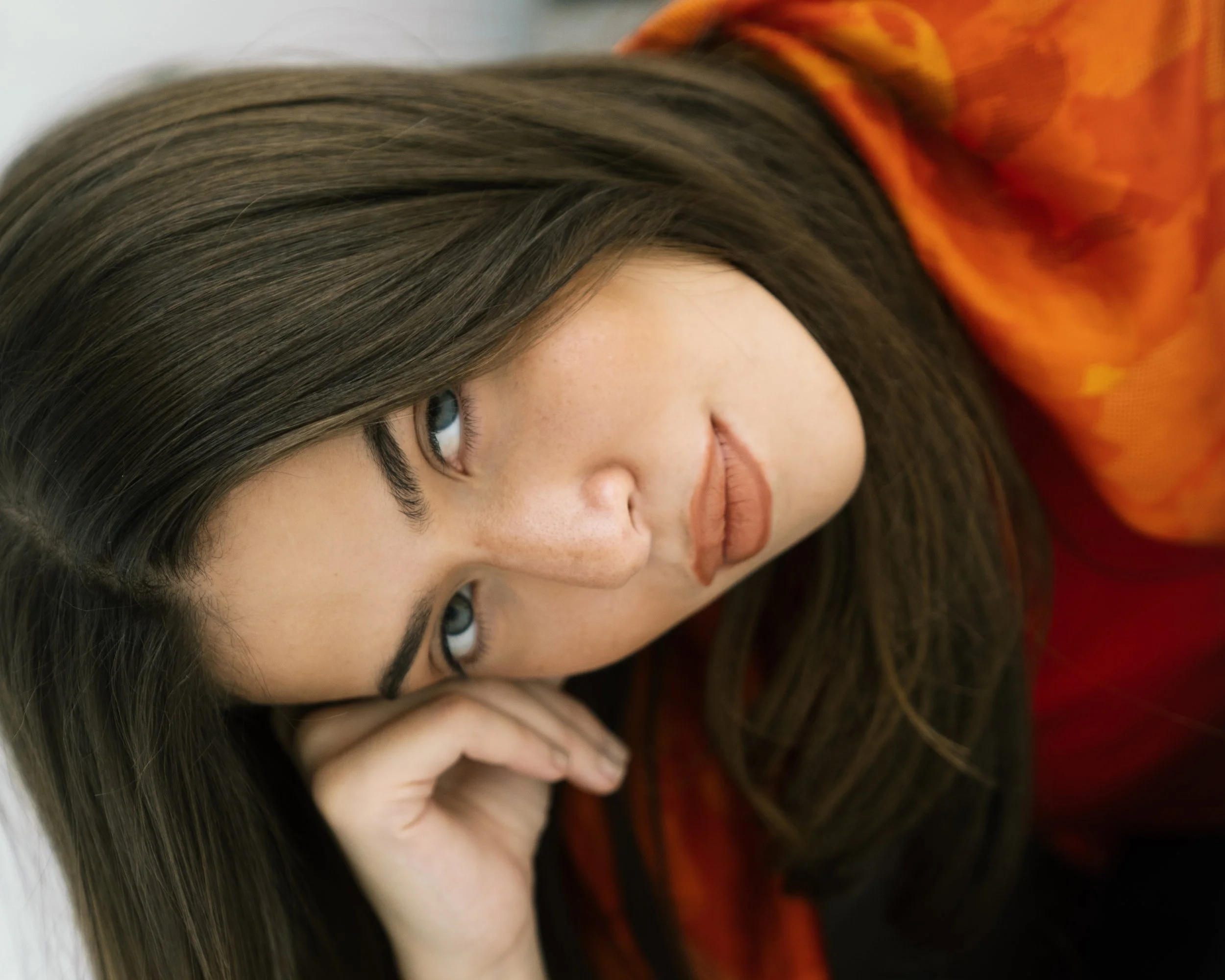 A woman with long brown hair lying on her side, resting her head on her hand, with her eyes looking at the camera.