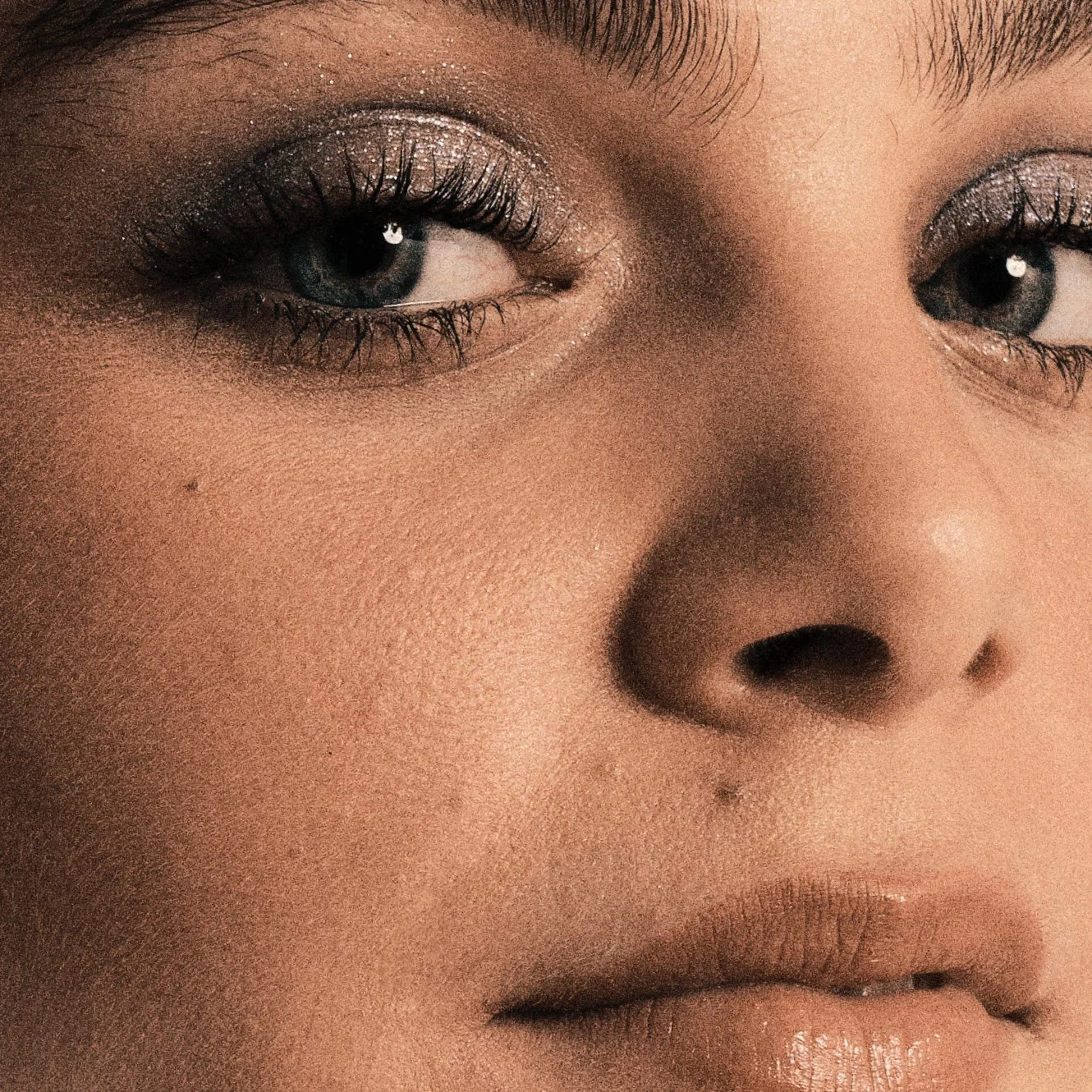 Close-up of a woman's face, highlighting her eyes with dark lashes and sparkly eye makeup, and her nose and lips.