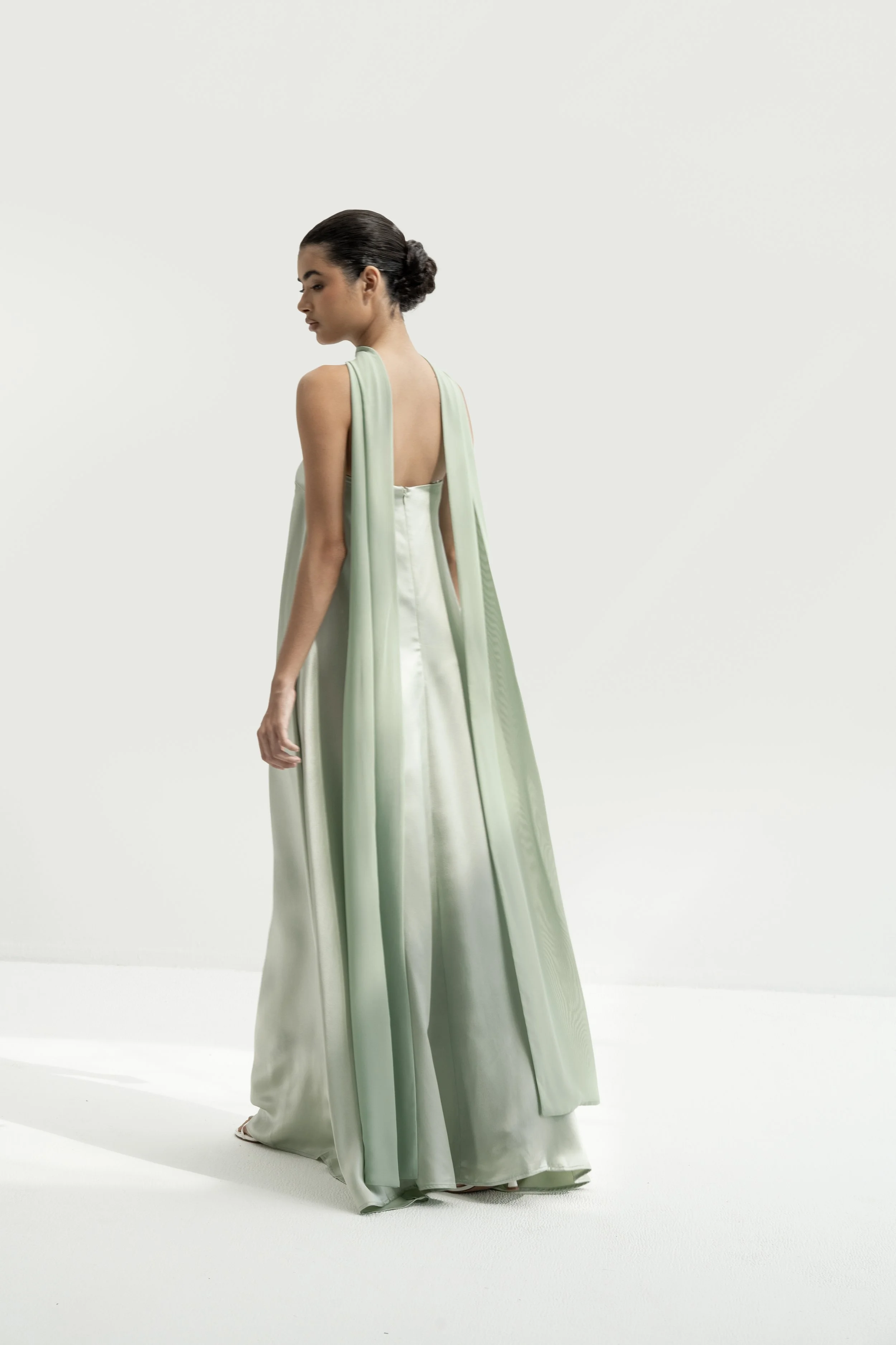 A woman in a flowing, elegant, satin gown with a gradient from white to light green, standing against a plain white background.