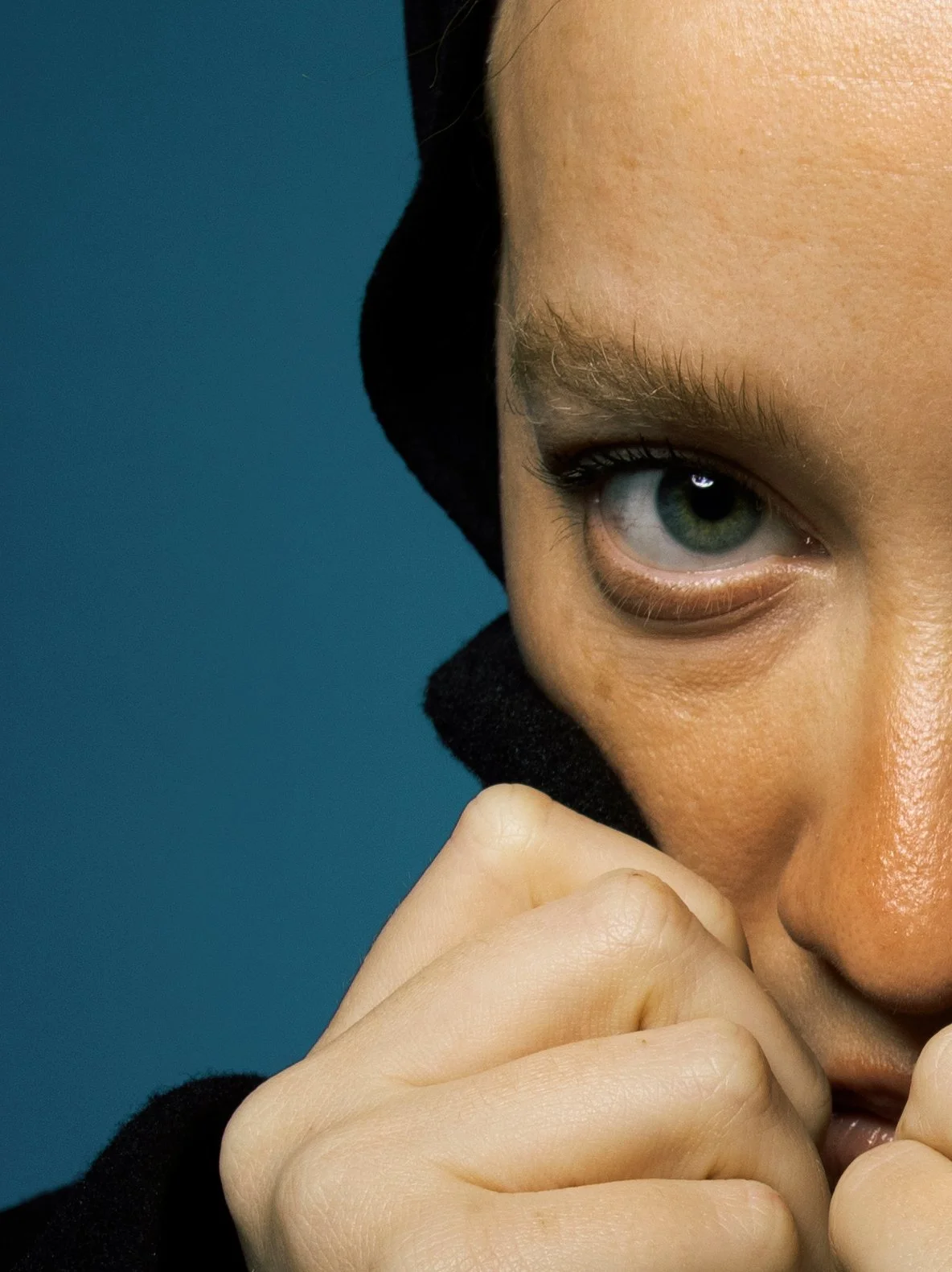 Close-up of a person's face showing one eye, nose, and hand covering part of their mouth, with a blue background.
