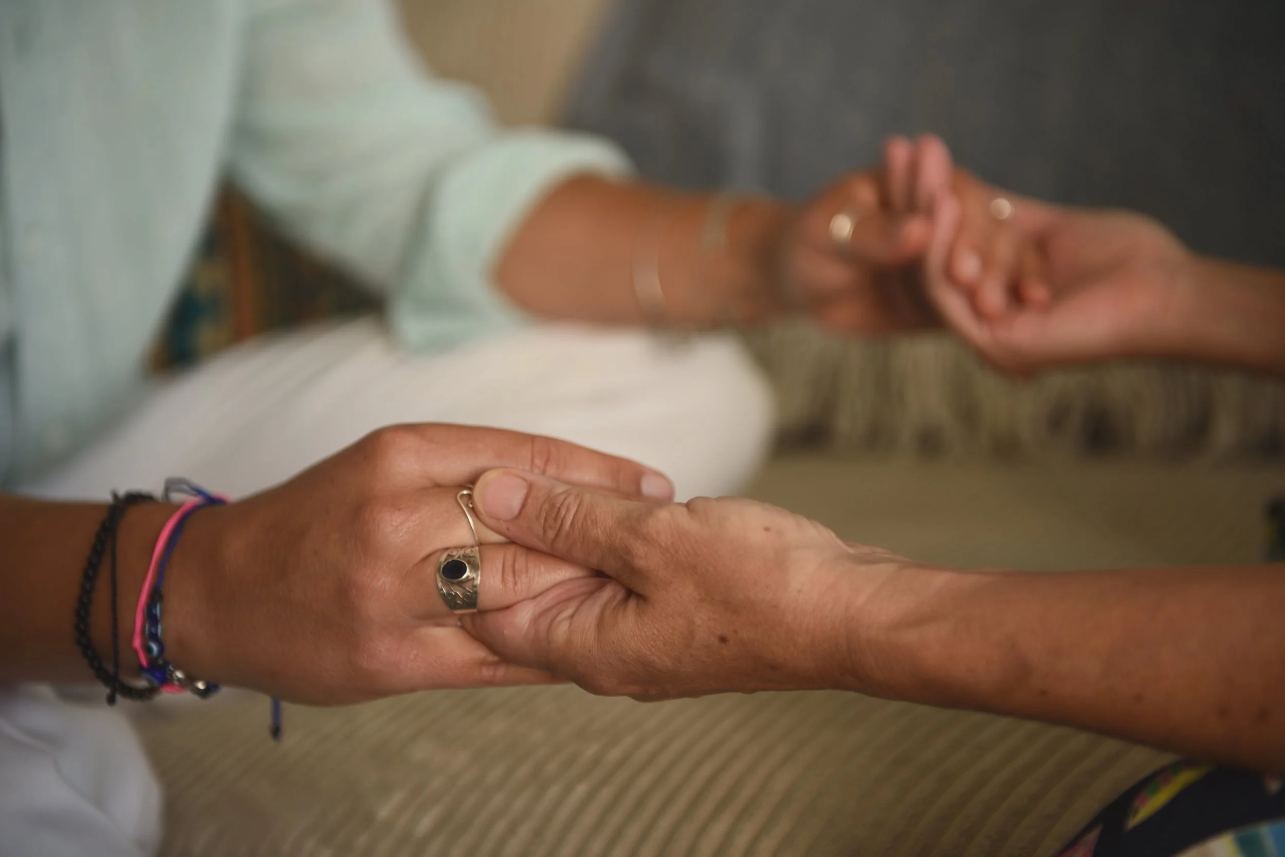 Two people holding hands, one with a ring and bracelets, gently clasping the other's hand in a comforting gesture.