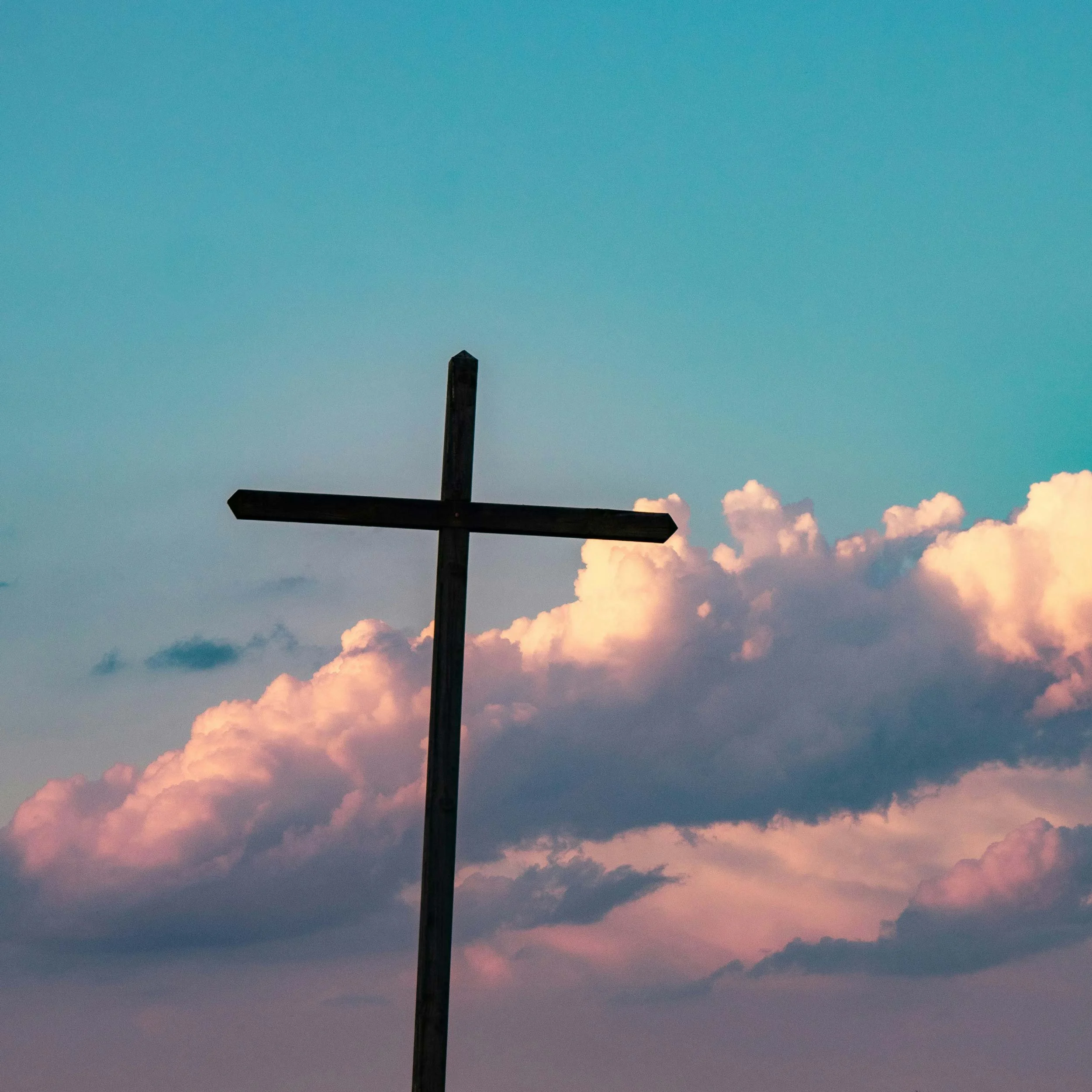 A silhouette of a wooden cross against a sky with pink and orange clouds during sunset.