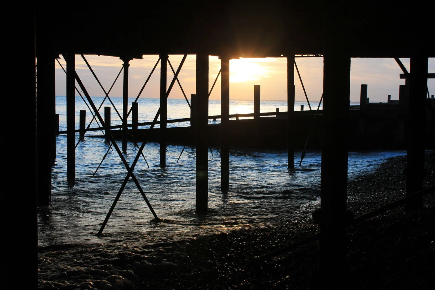 Sunset view through the understructure of a pier over the ocean.