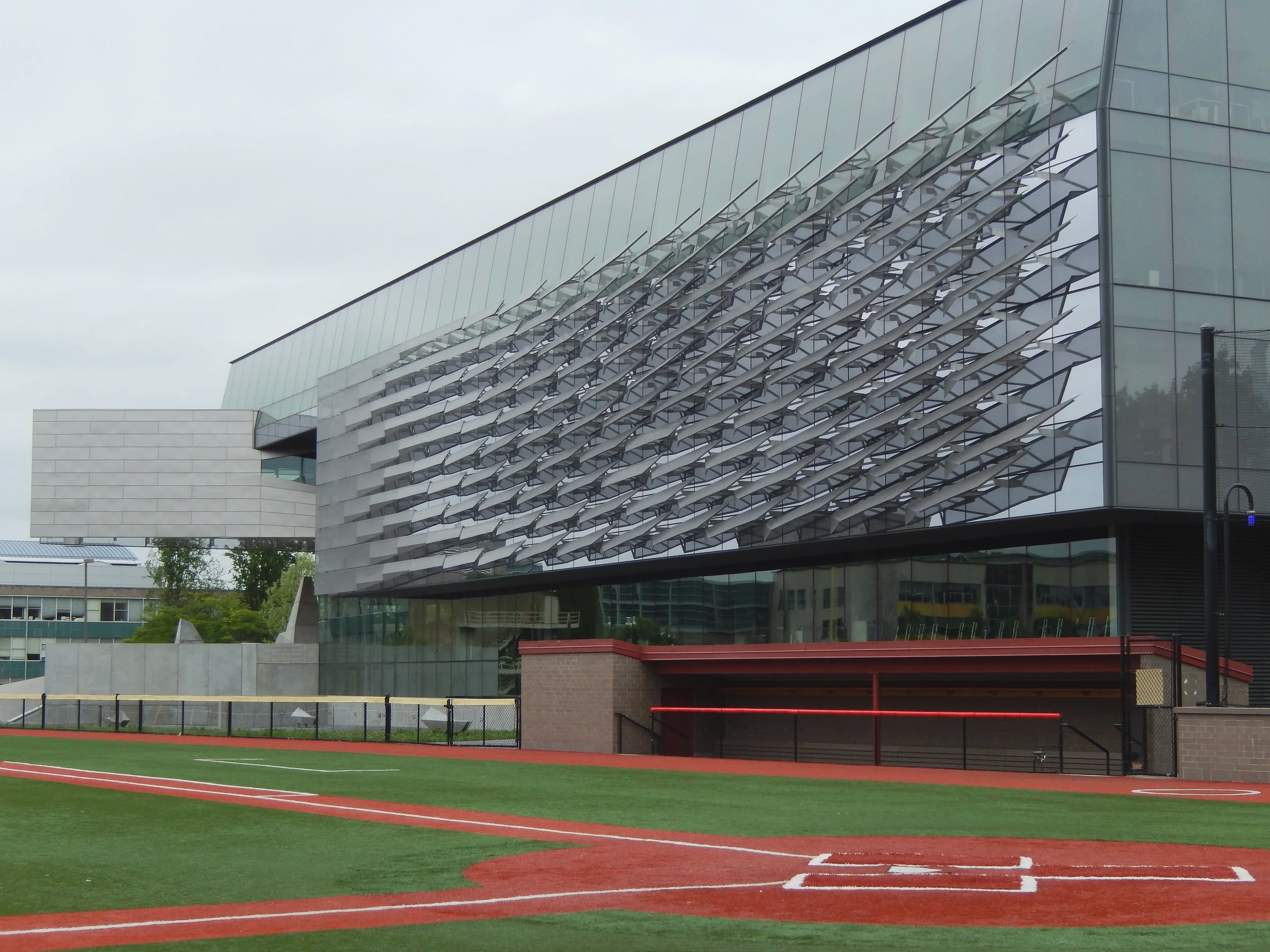 Modern sports stadium with a baseball field in the foreground and an architectural building with a unique metal and glass facade in the background.