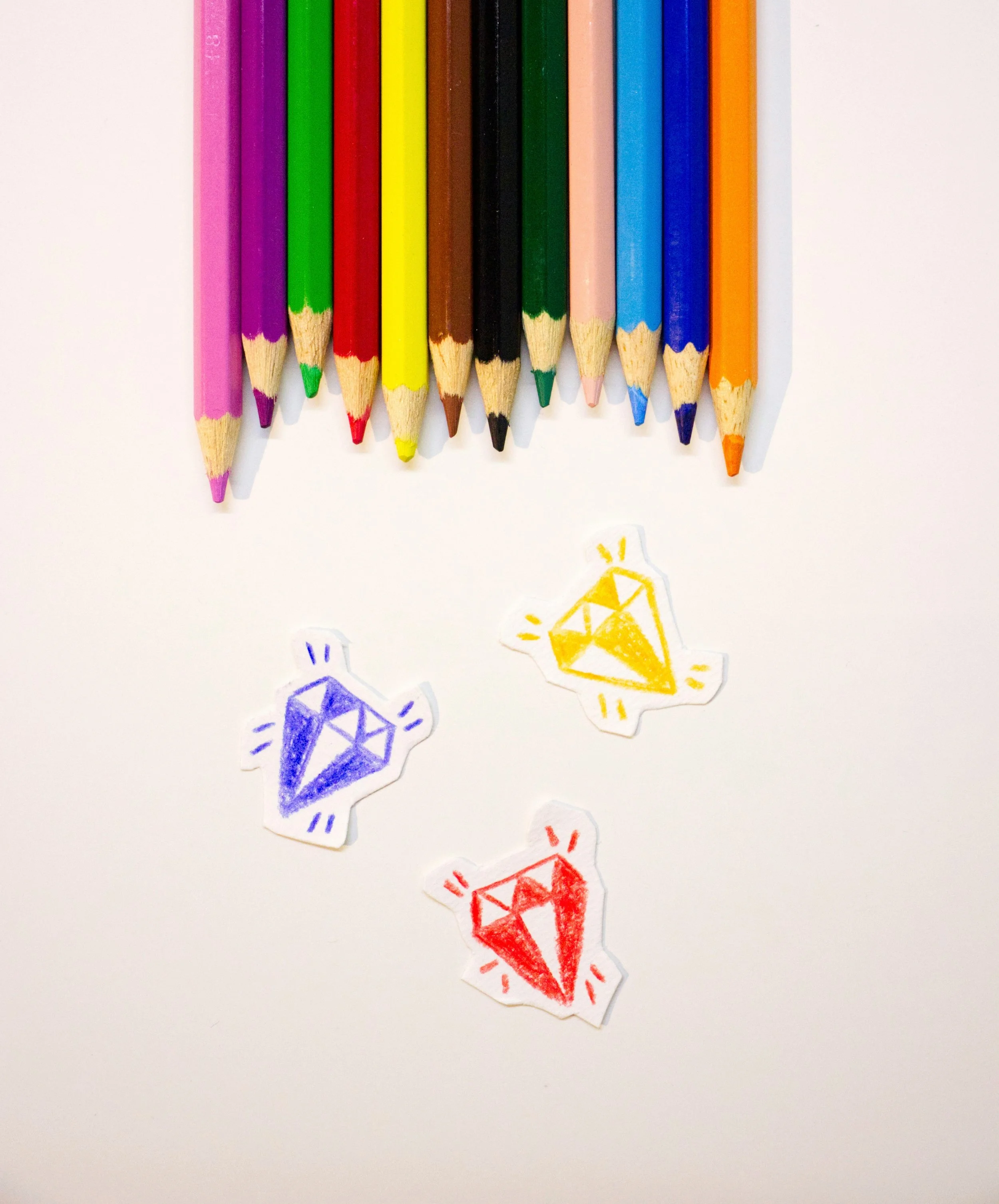 Colorful drawing of various colored pencils and paper cutouts of diamonds on white paper.