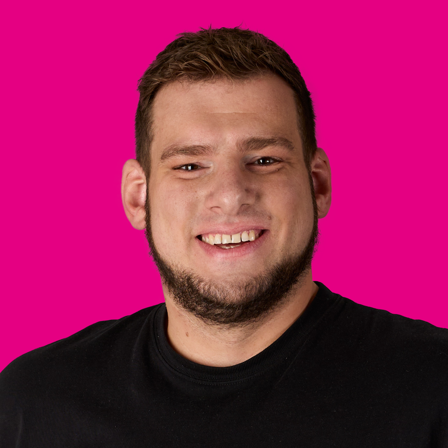 Lächelnder junger Mann mit dunklem T-Shirt vor einem pinken Hintergrund.