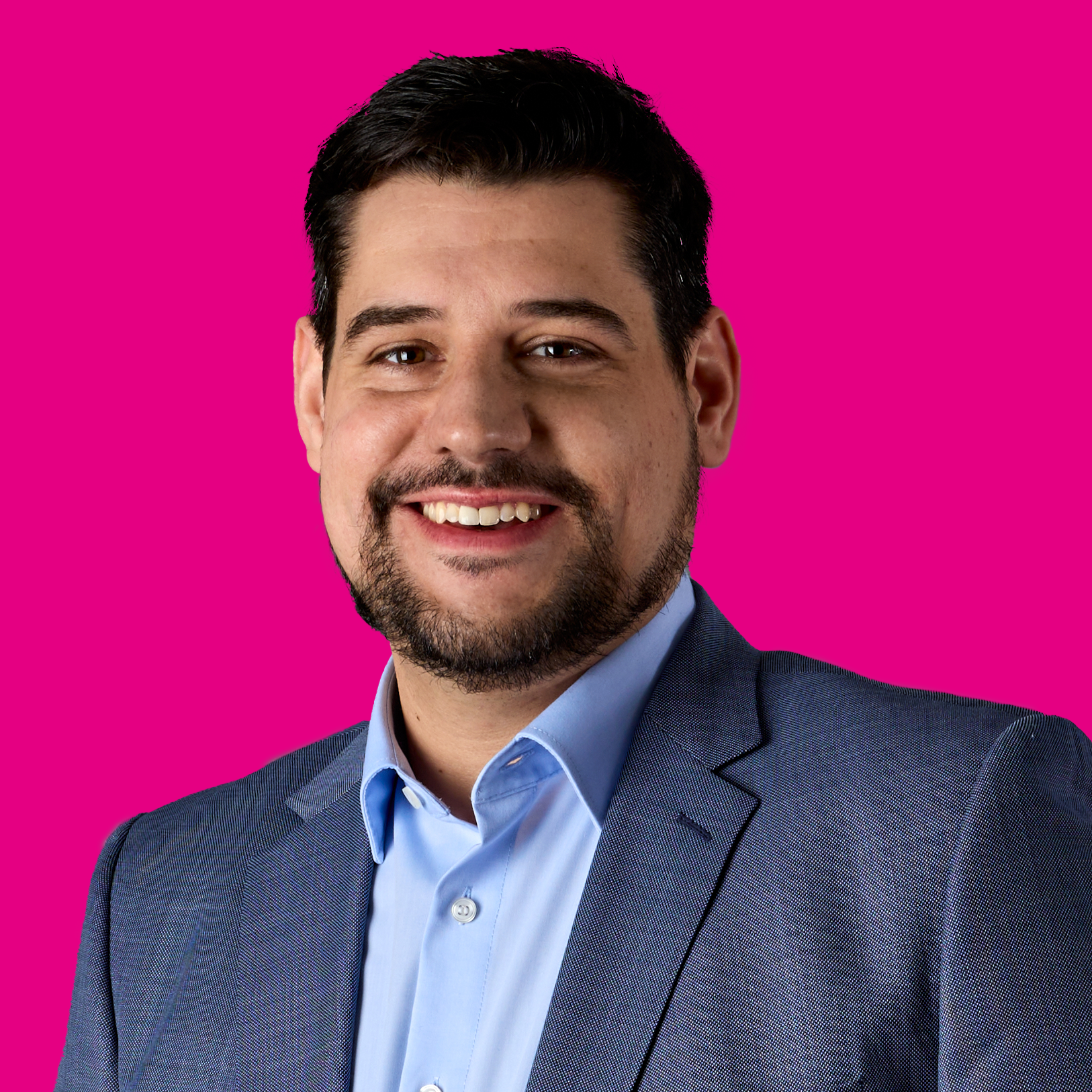 Porträt eines lächelnden Mannes in einem blauen Anzug vor pinkem Hintergrund.
