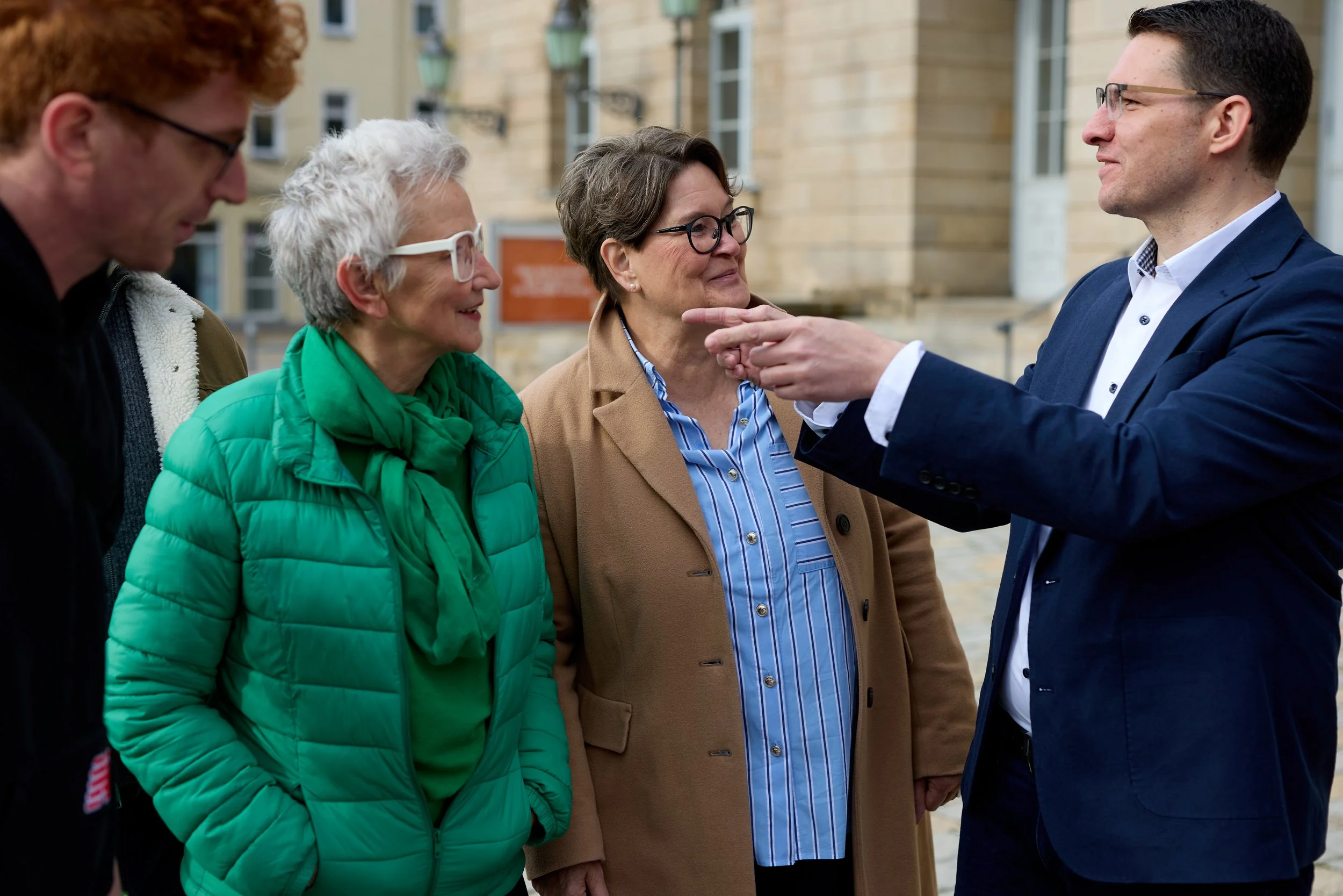 Fünf Menschen sprechen draußen, sie lachen und scheinen sich zu unterhalten.