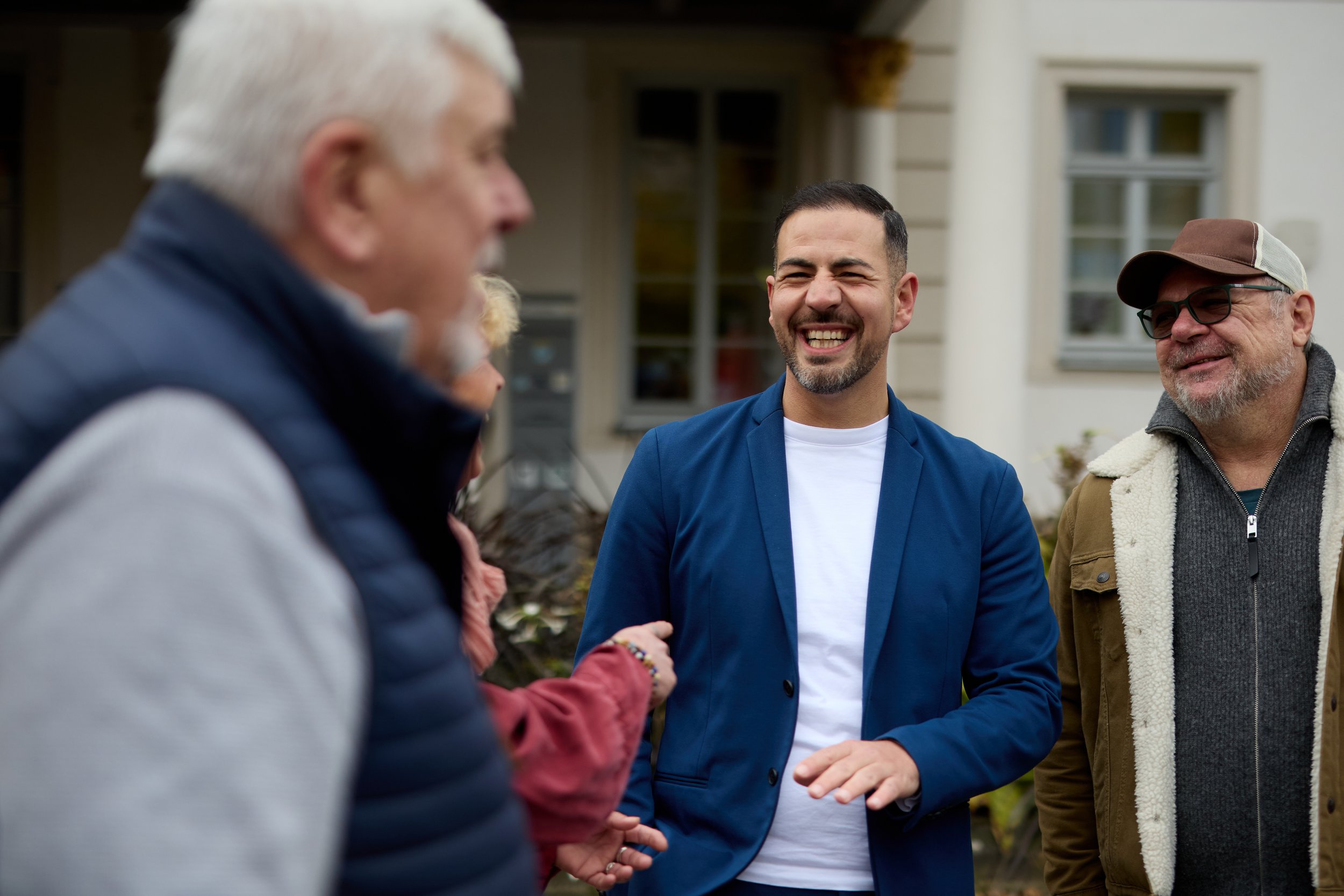 Menschen beim freundlichen Gespräch im Freien, lächelnd, im Hintergrund ein Haus.