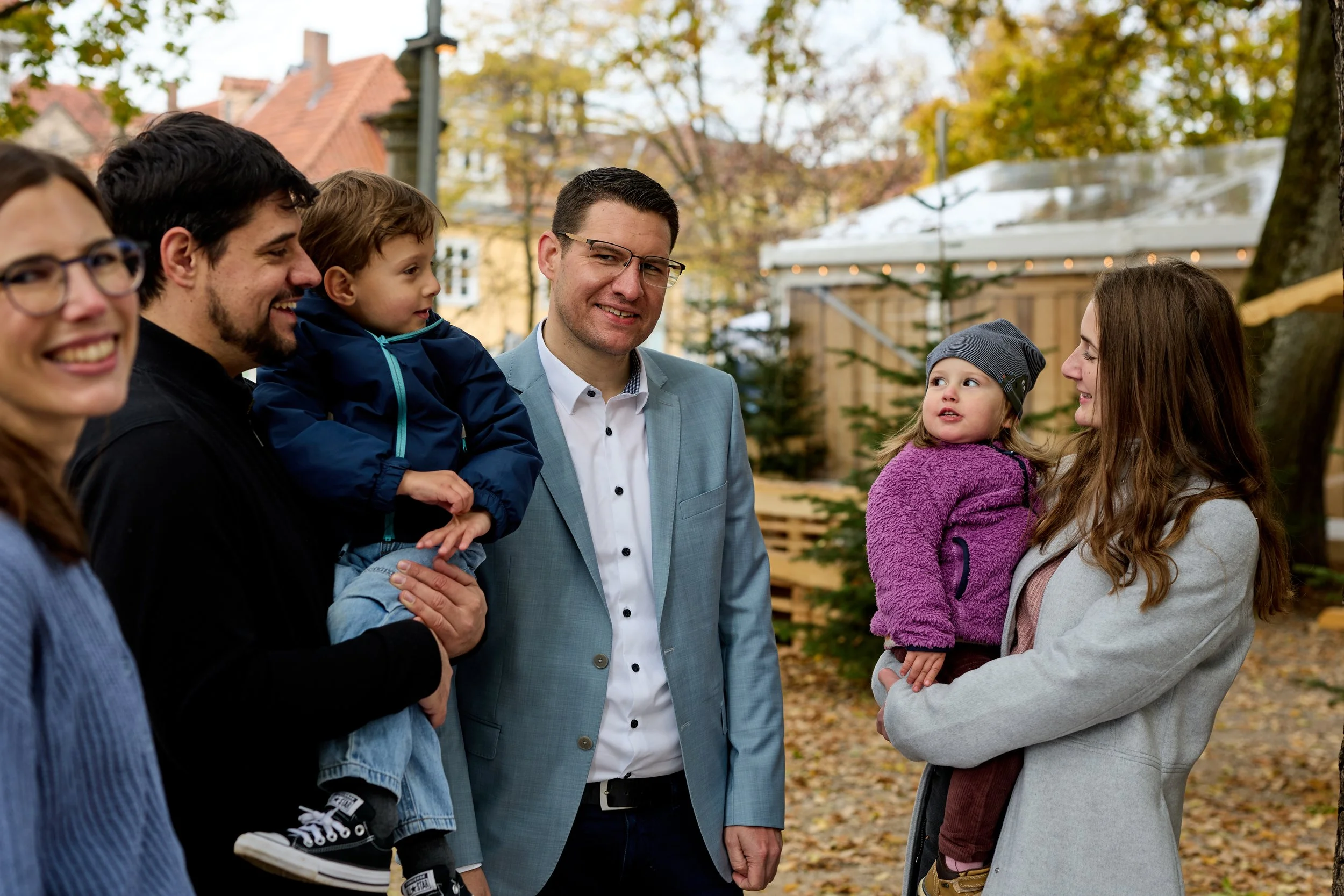 Familie beim Treffen im Freien im Herbst, mit bunten Blättern und Weihnachtsbaum im Hintergrund.