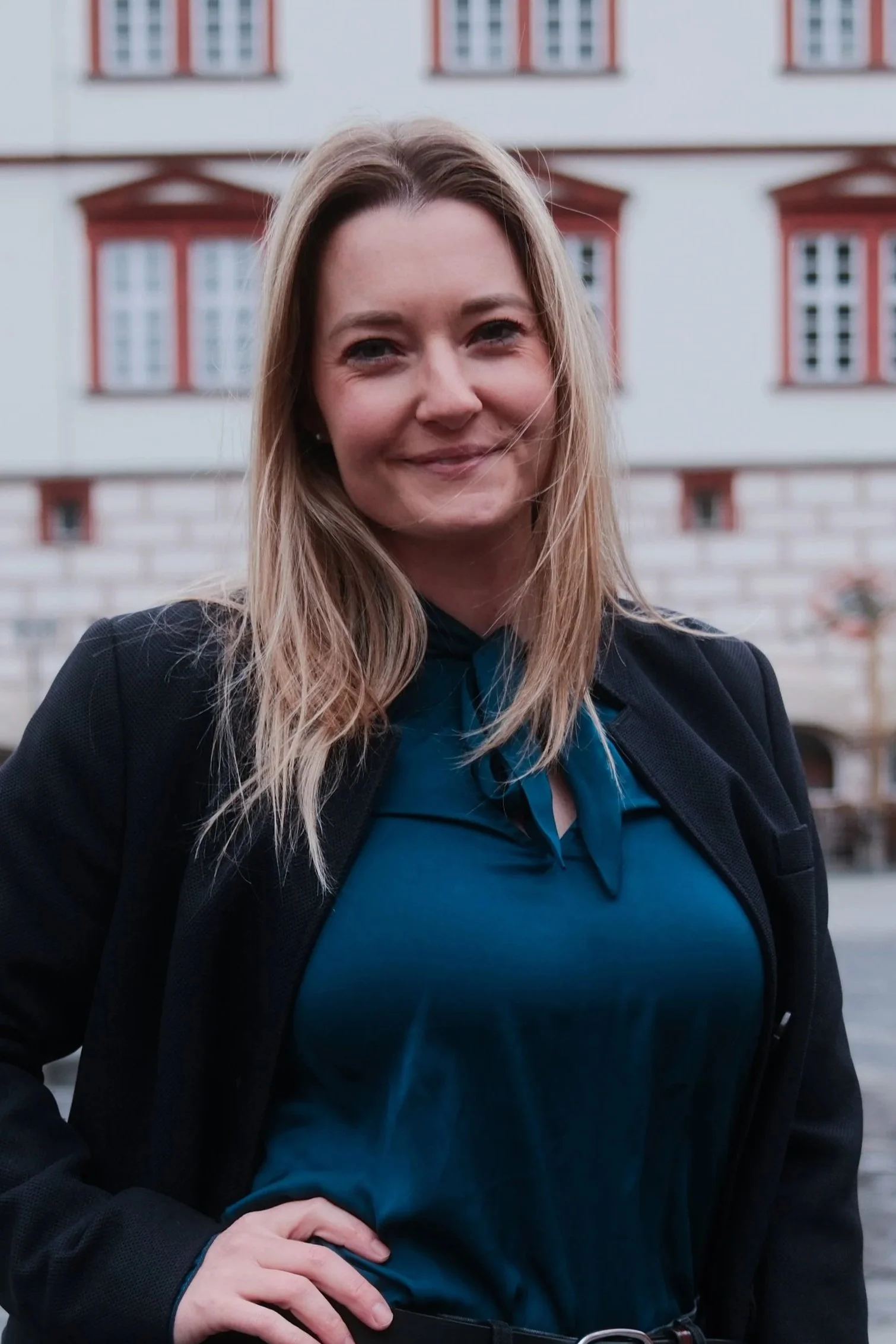Porträt einer lächelnden Frau vor pinkem Hintergrund, trägt schwarze Jacke und rotes Oberteil mit Leopardenmuster.
