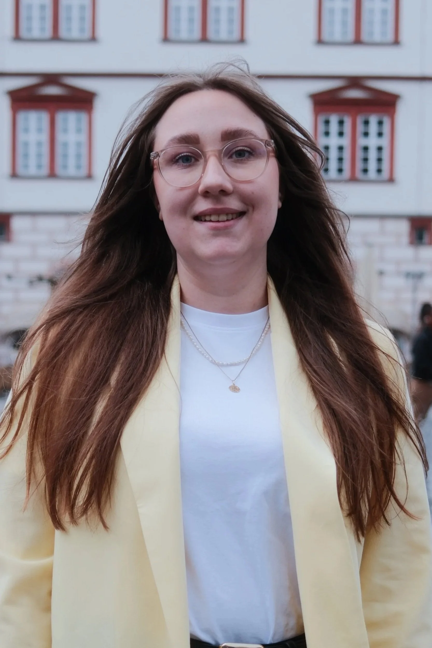 Nahaufnahme eines lachenden jungen Mädchens mit Brille vor pinkem Hintergrund.