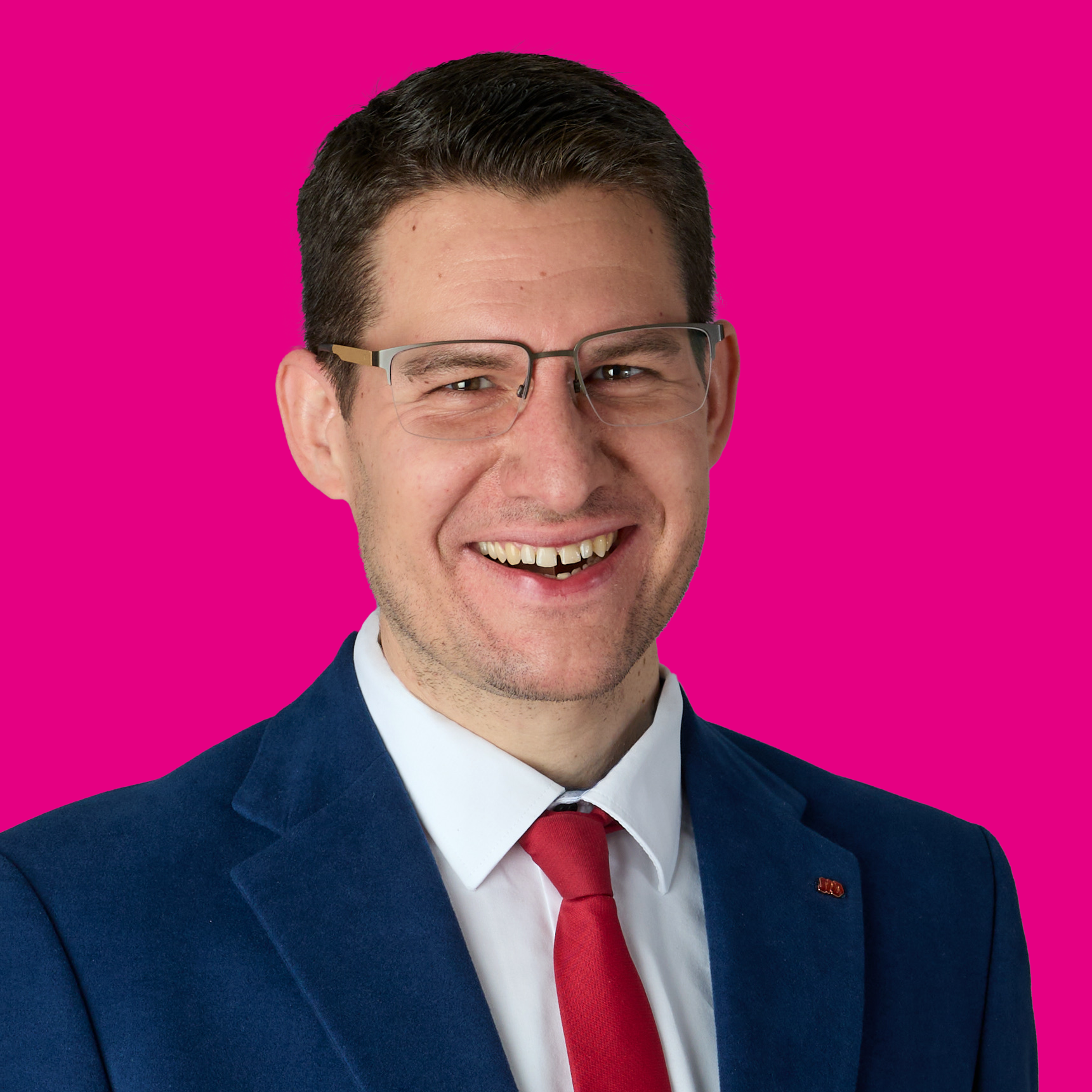 Mann in Businesskleidung mit Brille lächelt vor pinkem Hintergrund.