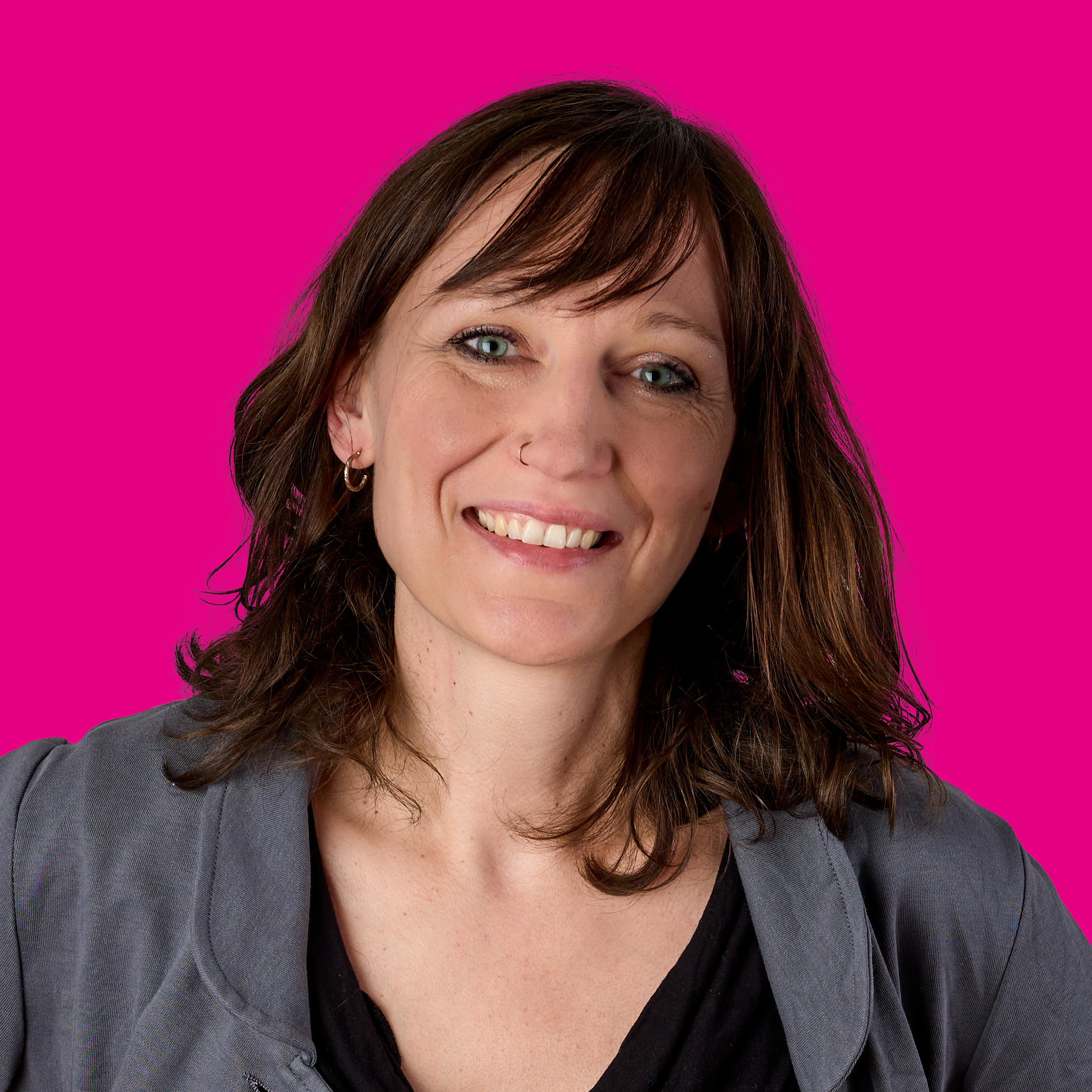 Eine lächelnde Frau mit braunen Haaren vor einem pinken Hintergrund.