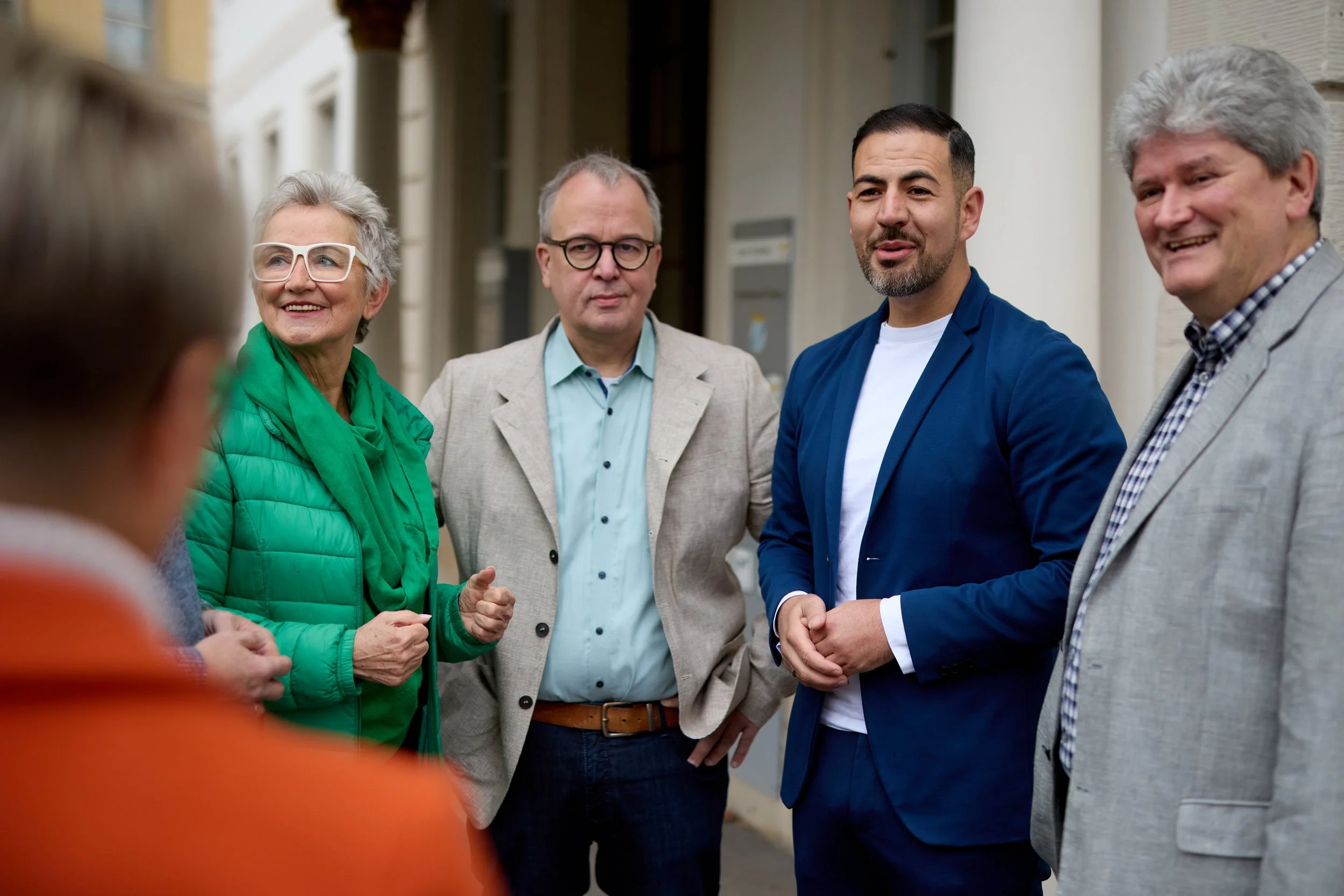 Fünf Personen im Gespräch vor einem Gebäude, lächelnd und diskutierend.