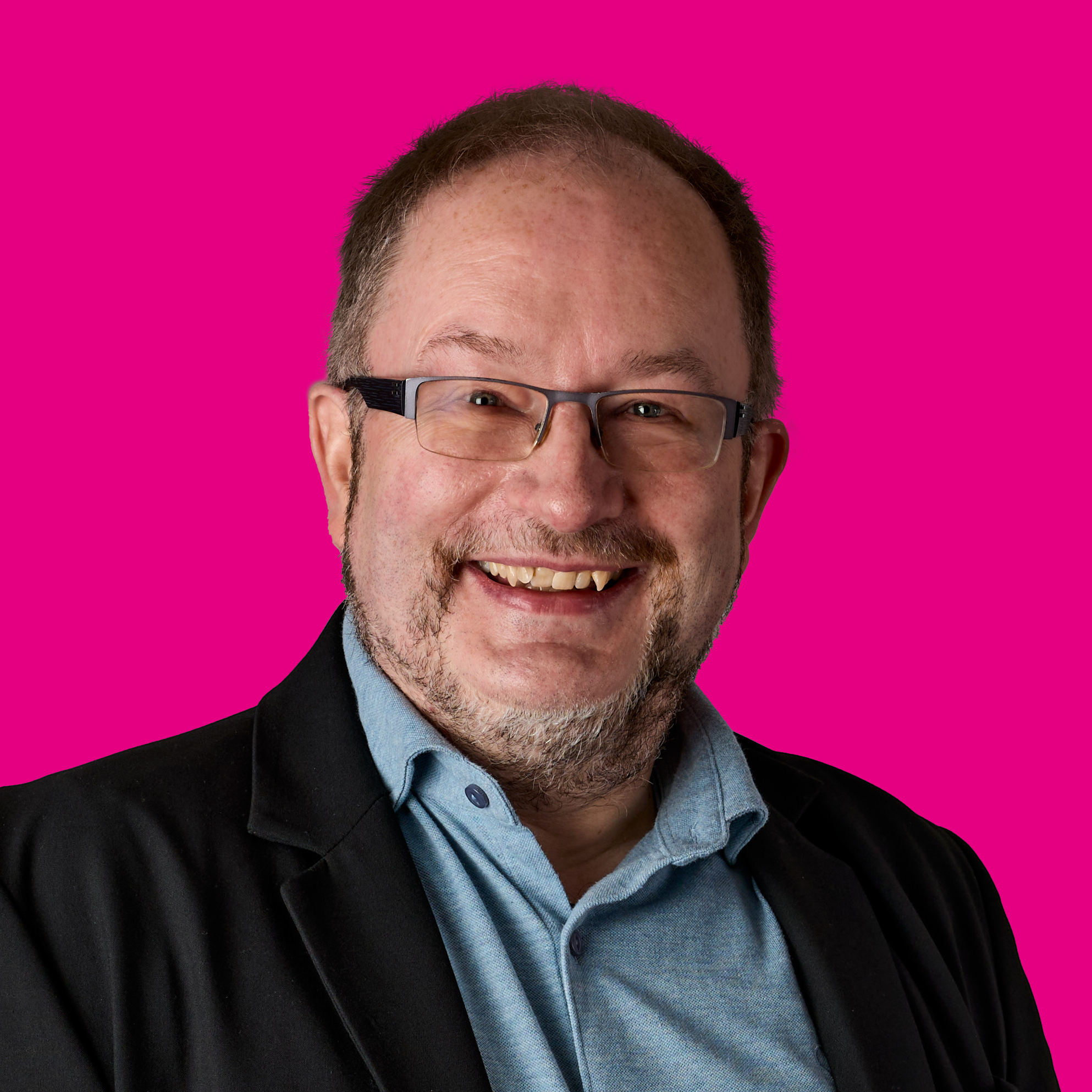 Porträt eines lächelnden Mannes mit Brille vor pinkem Hintergrund.