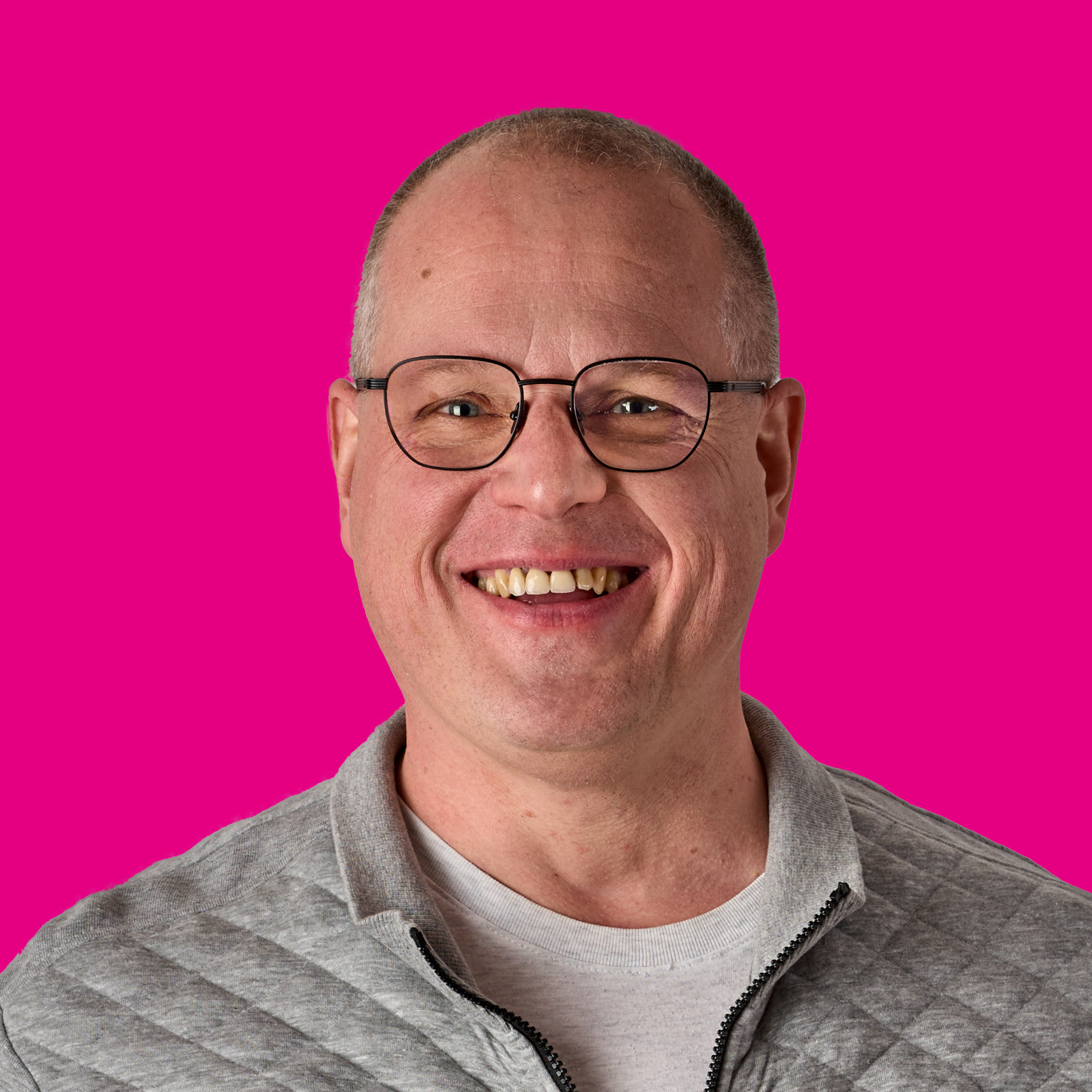 Lächelnder Mann mit Brille vor pinkem Hintergrund