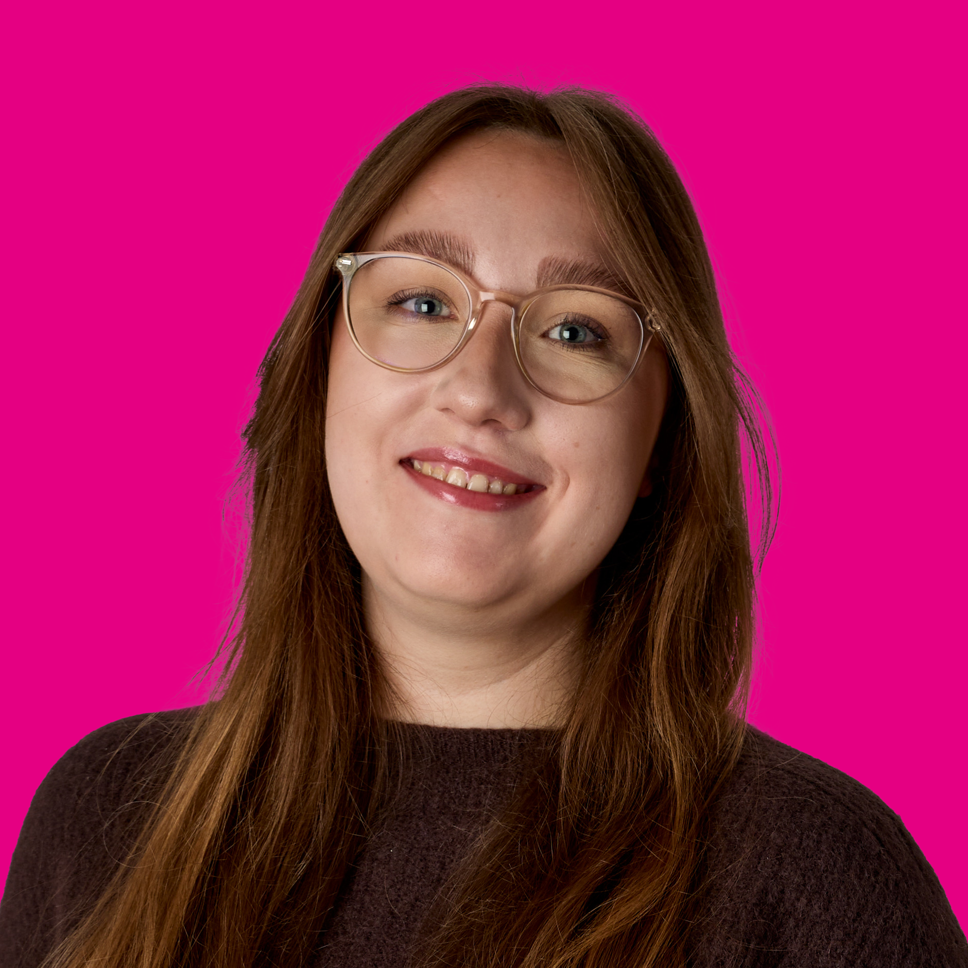 Ein junges Mädchen mit Brille und braunem Haar vor pinkem Hintergrund, das lächelt.