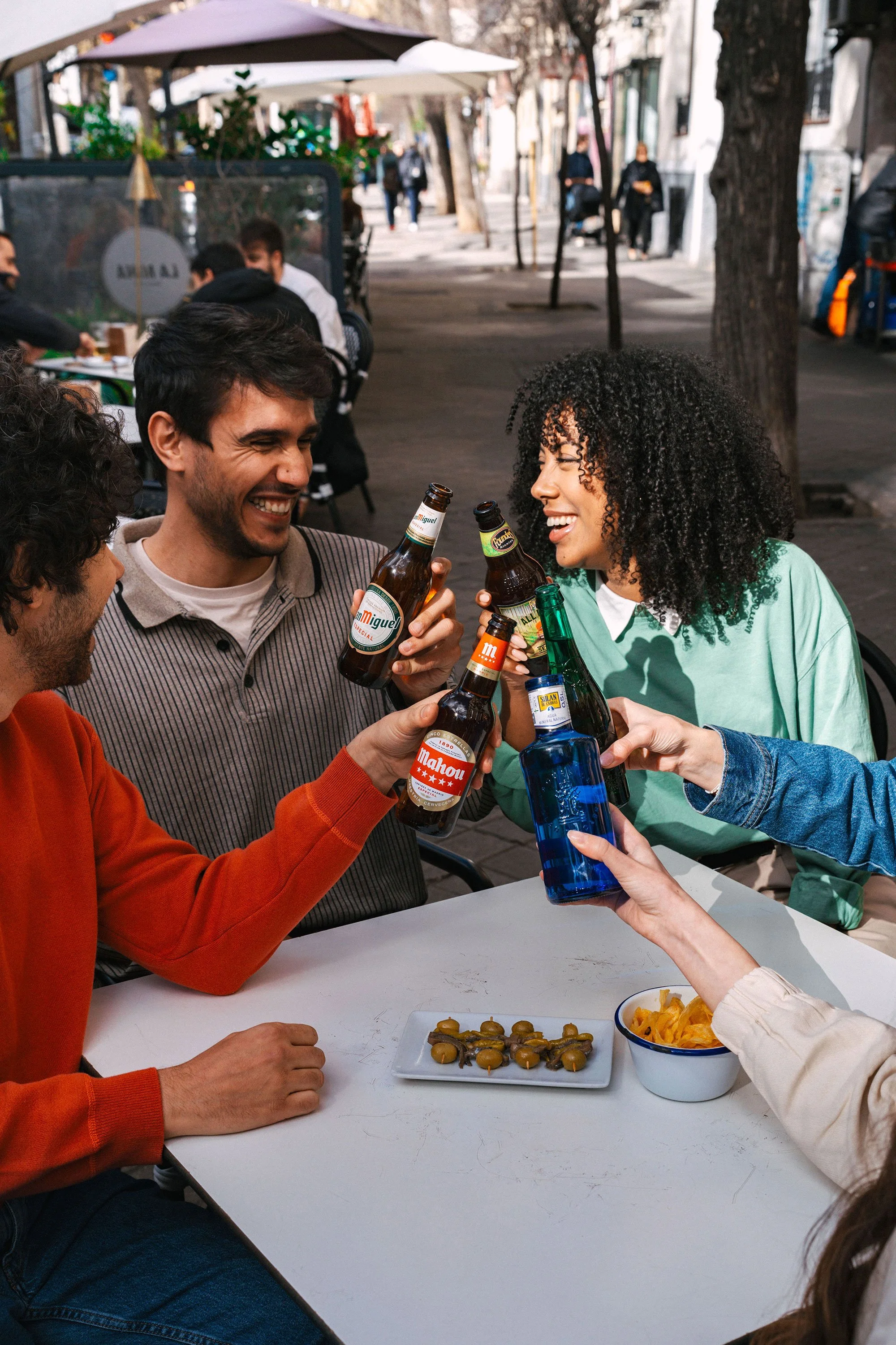 Grupo de amigos brindando con cervezas en una terraza al aire libre, disfrutando y sonriendo.