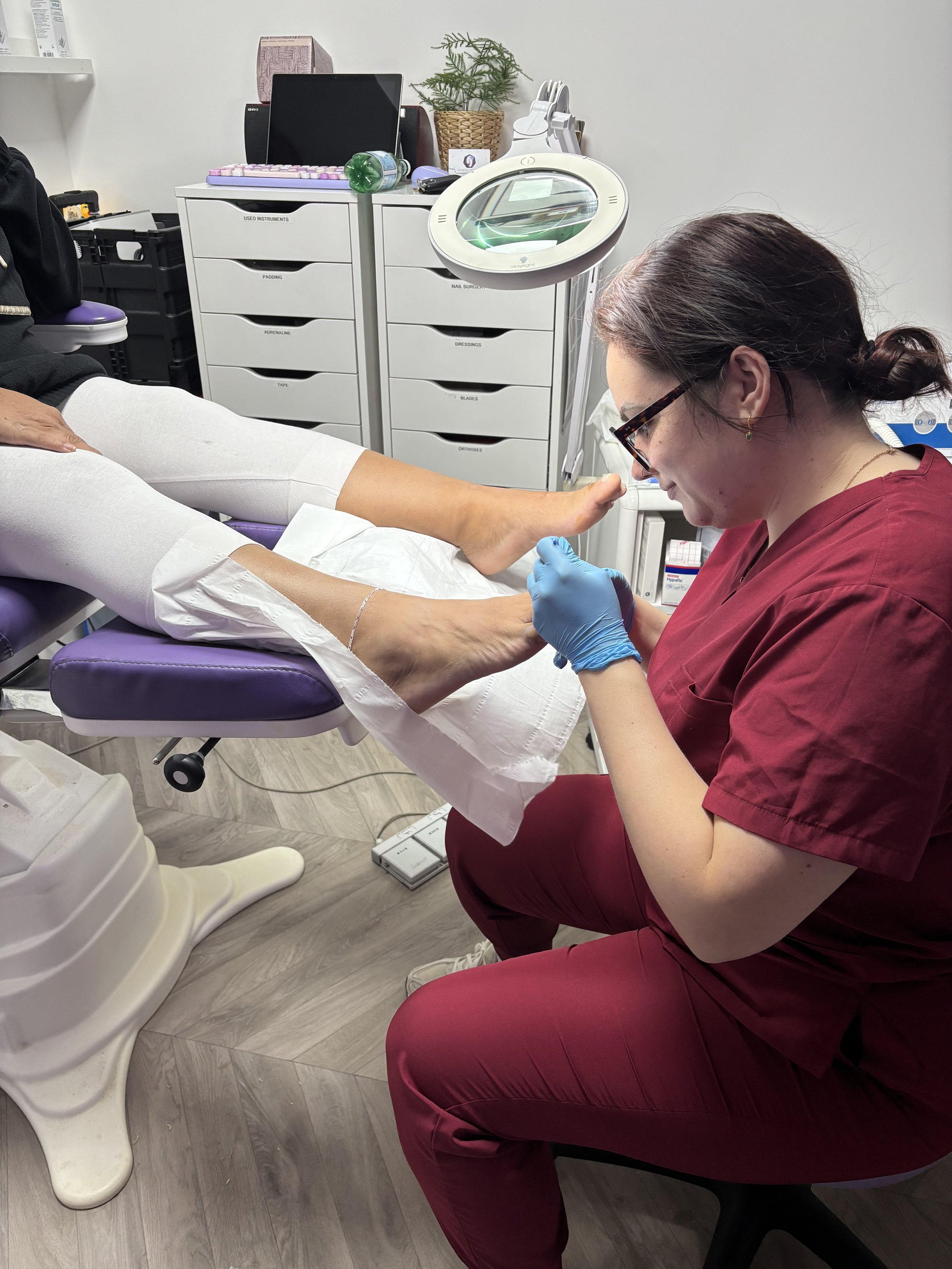 A nurse examining a patient's foot in a medical office, with medical supplies and equipment in the background.