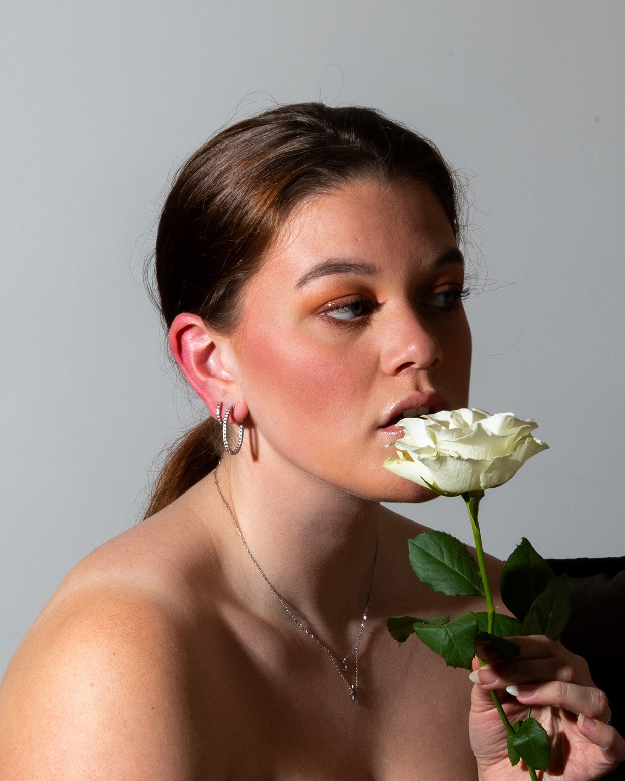 Vrouw met bruine haren houdt witte roos bij haar gezicht tegen grijze achtergrond – artistieke portretfotografie studio