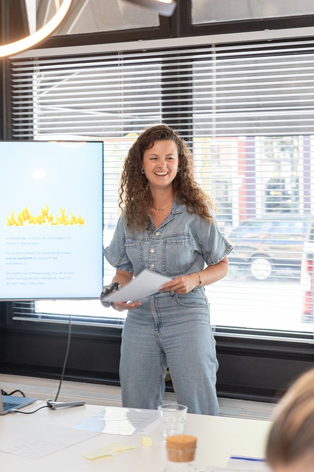Vrouw met krullend haar in denim outfit geeft presentatie in modern kantoor – zakelijke portretfotografie