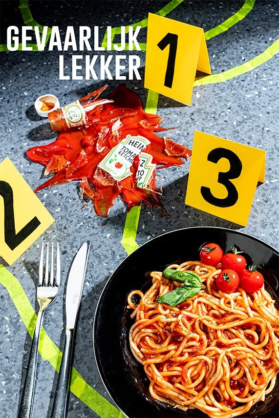 Kapotte ketchup fles naast bord spaghetti met cherrytomaten en basilicum, met waarschuwingsmarkers met de tekst 'Gevaarlijk Lekker' – creatieve food fotografie conceptueel