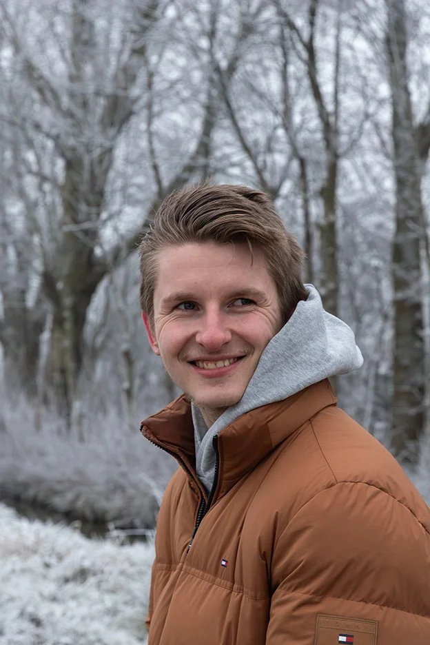 Jongeman lachend in winter met besneeuwde bomen op achtergrond – portretfotografie buiten winter