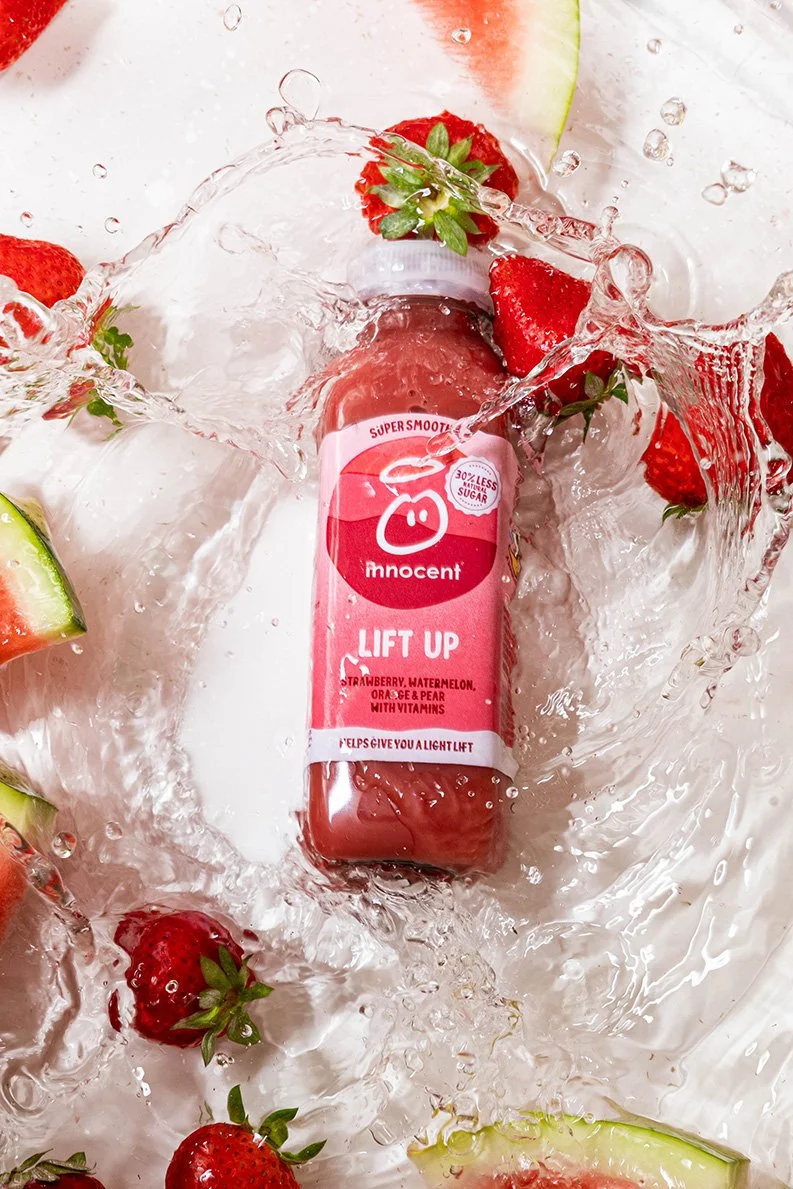 Roze fles “Innocent Lift Up” drankje met aardbeien en watermeloen, omringd door spattend water – commerciële drank productfotografie