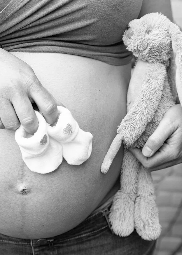 Zwangere vrouw met babysokjes en knuffel bij haar buik – zwangerschapsfotografie detail